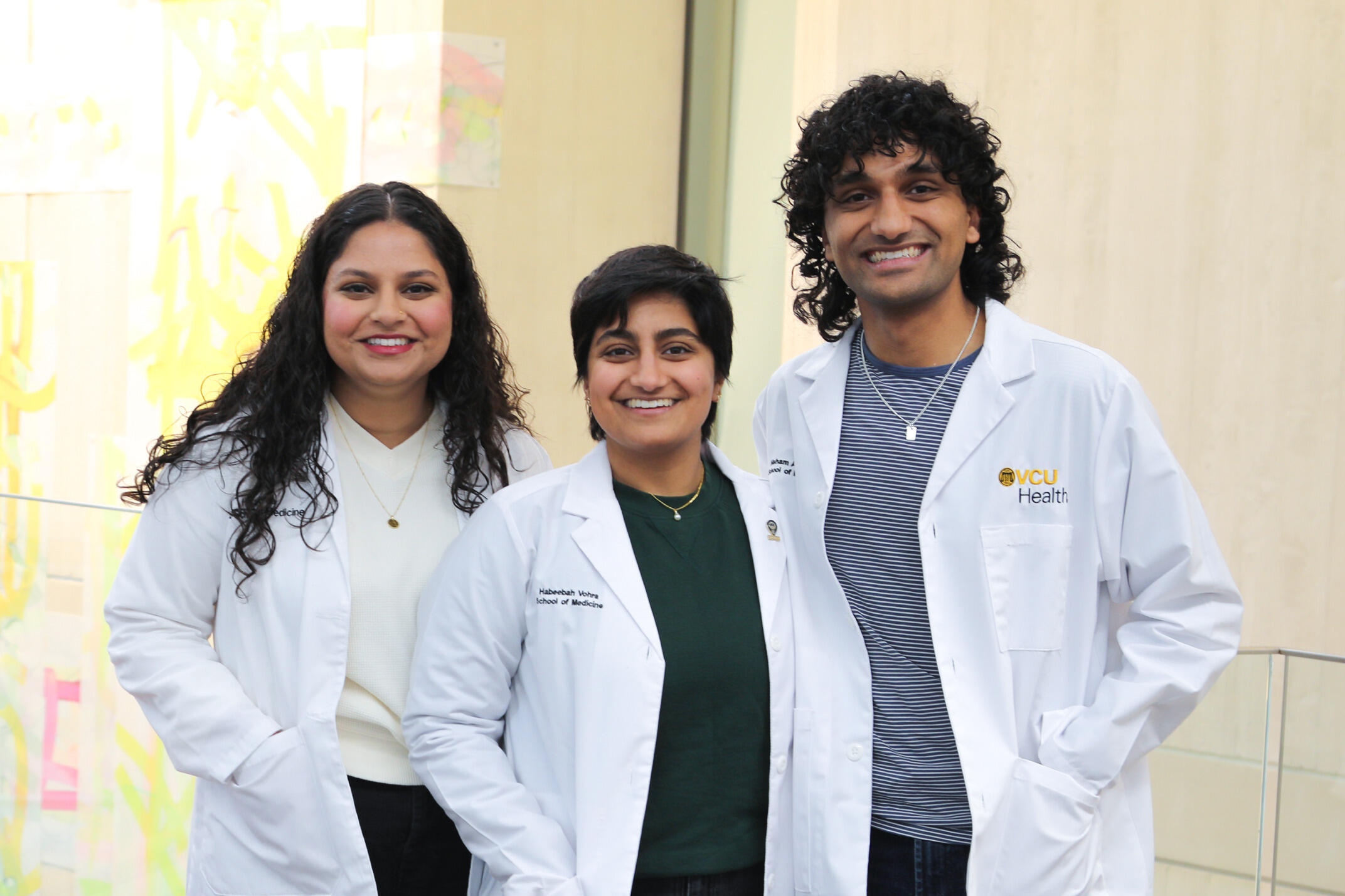 A photo of three people wearing whie lab coats and smiling. 