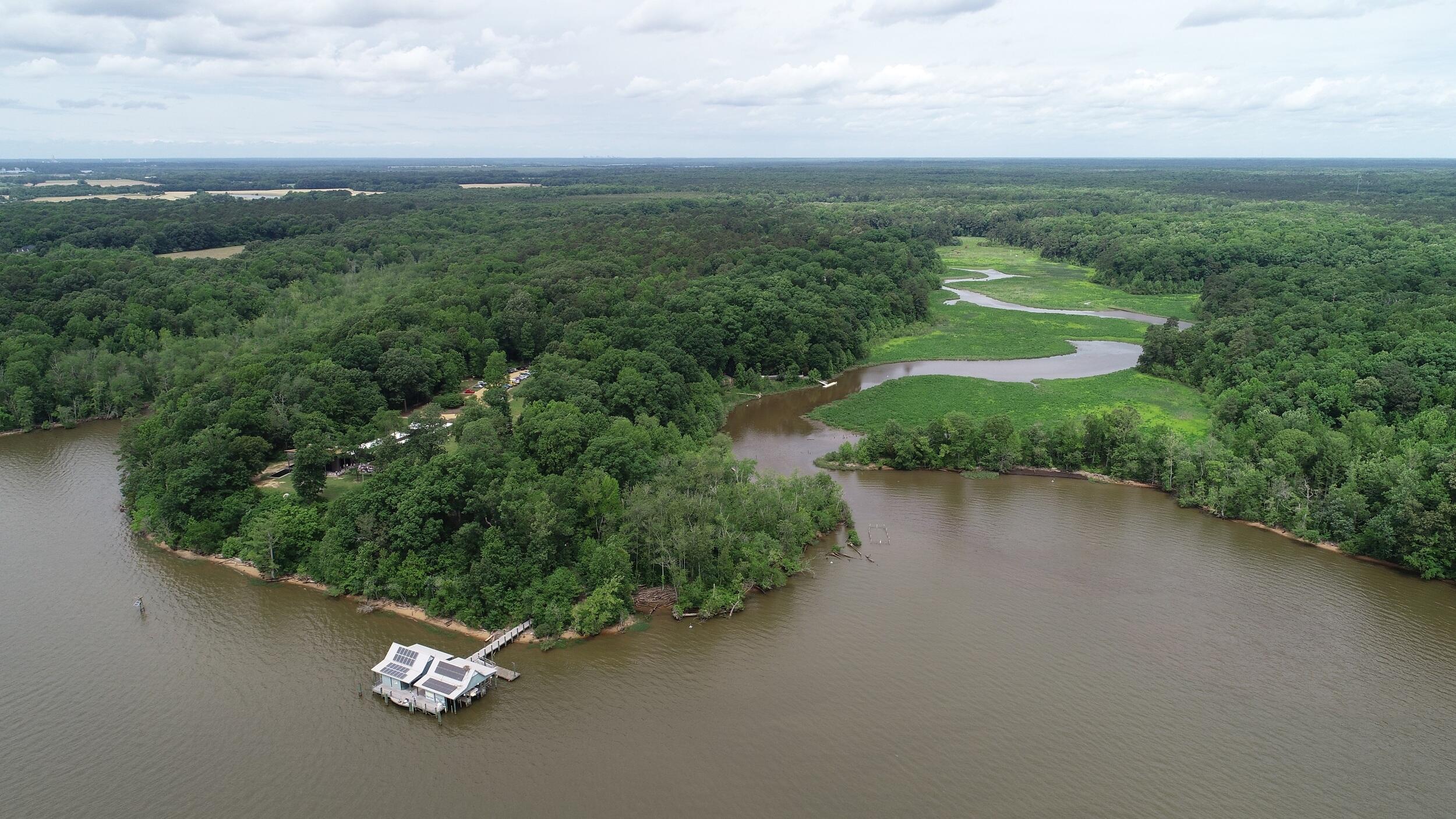 An aerial photo of the James River next to a forest and wetland. On the treeline is a doc leading to a building. 