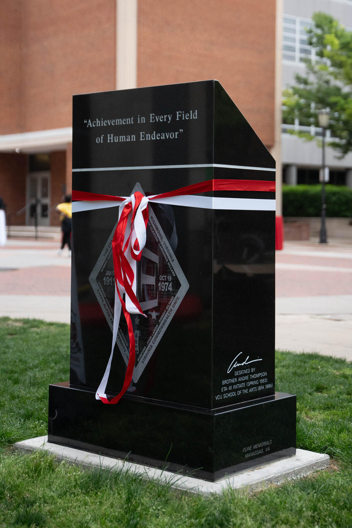 A photo of a black marble monument with white and red ribbons wrapped around it. 