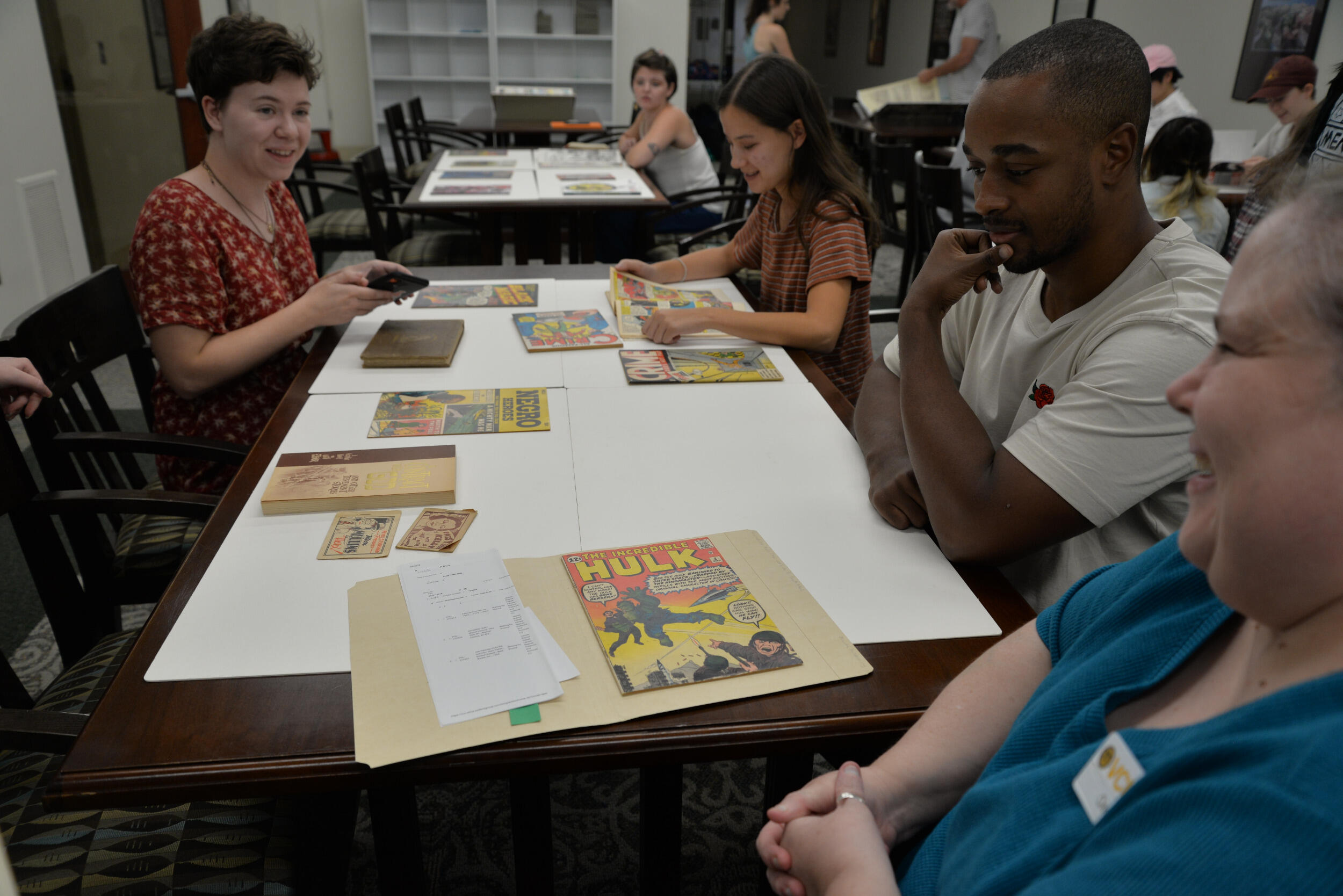 Students sit at a long table with comics issues on the table. Cindy Jackson is smiling in the foreground at the end of the table.