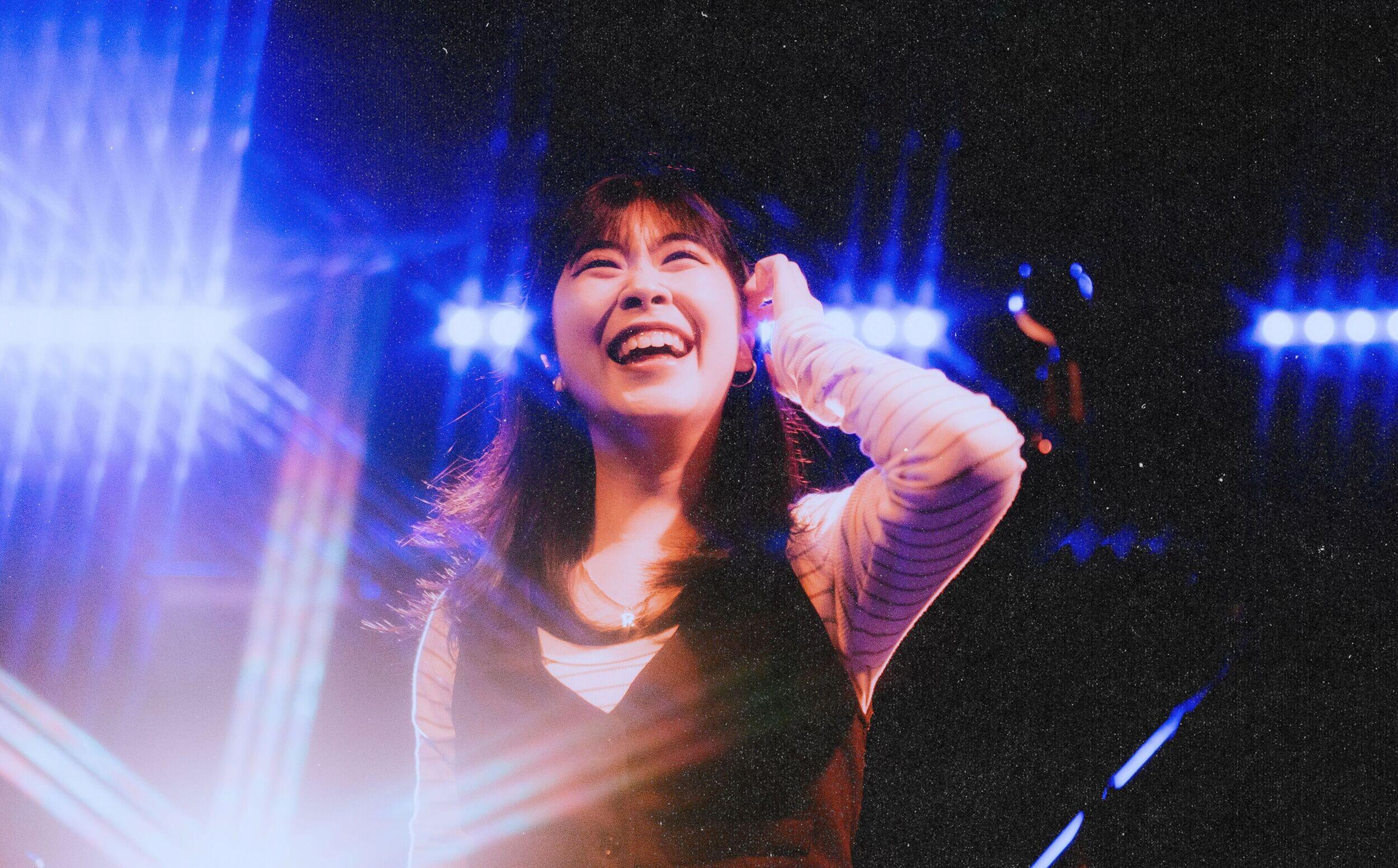 A smiling woman on stage with bright lights around her.