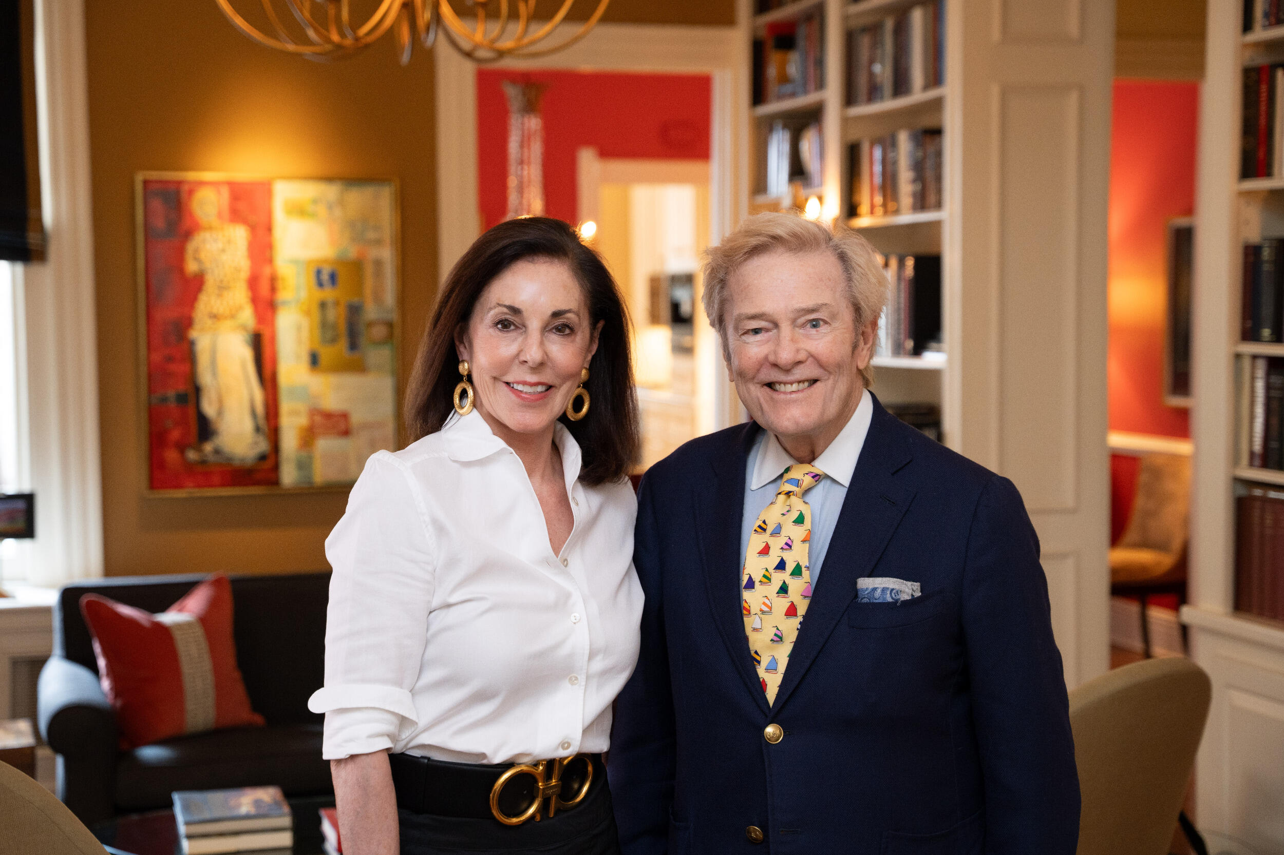 A man and a woman stand next to each other and smile in a living room with art on the walls
