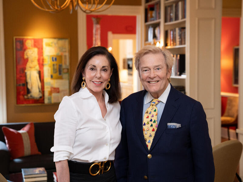 A man and a woman stand next to each other and smile in a living room with art on the walls