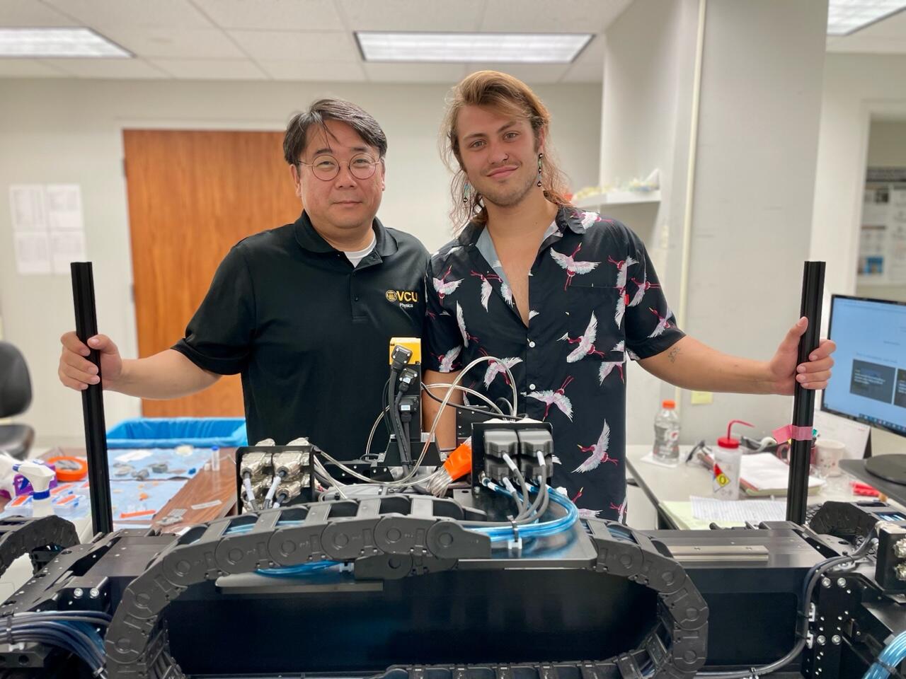 A photo of two men standing next to each other in front of testing equipment