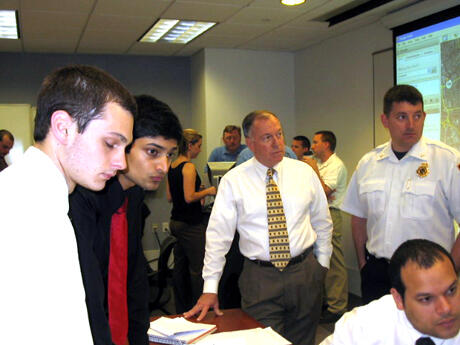 Senior Andrew Campo, senior Karan Singh, Associate Professor William Parrish and Henrico County Fire Battalion Chief Mike Cox react to a new development in the exercise.  L-3 Communications Services Group, a communications and surveillance products and services company, supported the exercise with its modeling and simulation software to help students manage regional emergency response assets as they established police road blocks, coordinated evacuations and directed fire and EMS response.  Photo by Mike Porter, University Communications and Public Relations