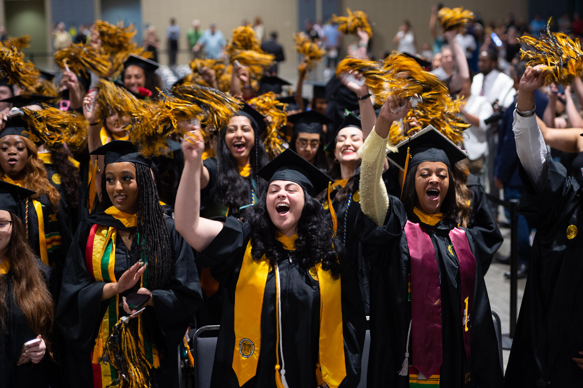 Graduates wave black and gold pom poms.