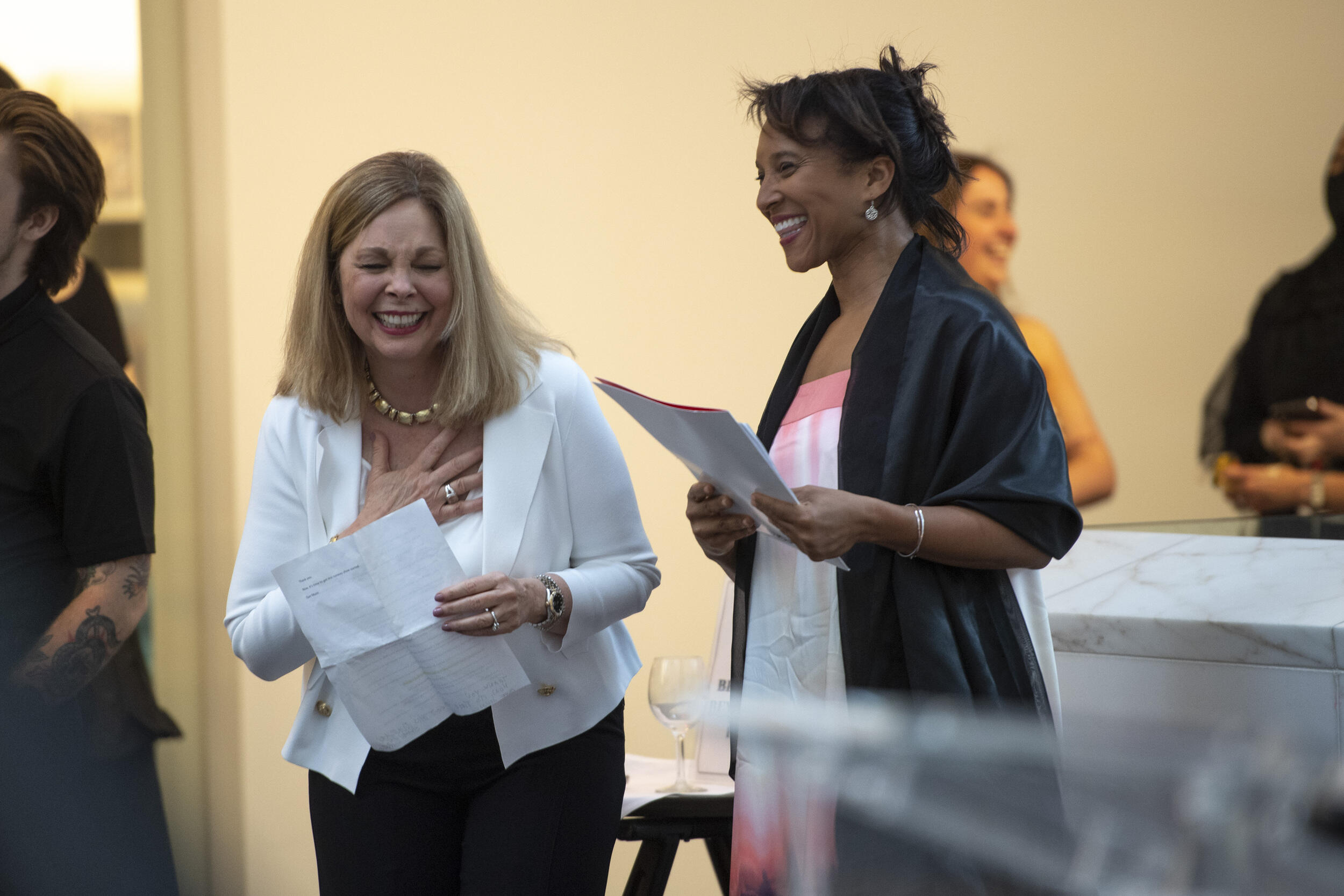 Left to right: Deidra Arrington and Carmenita Higginbotham holding each other and holding papers while laughing 