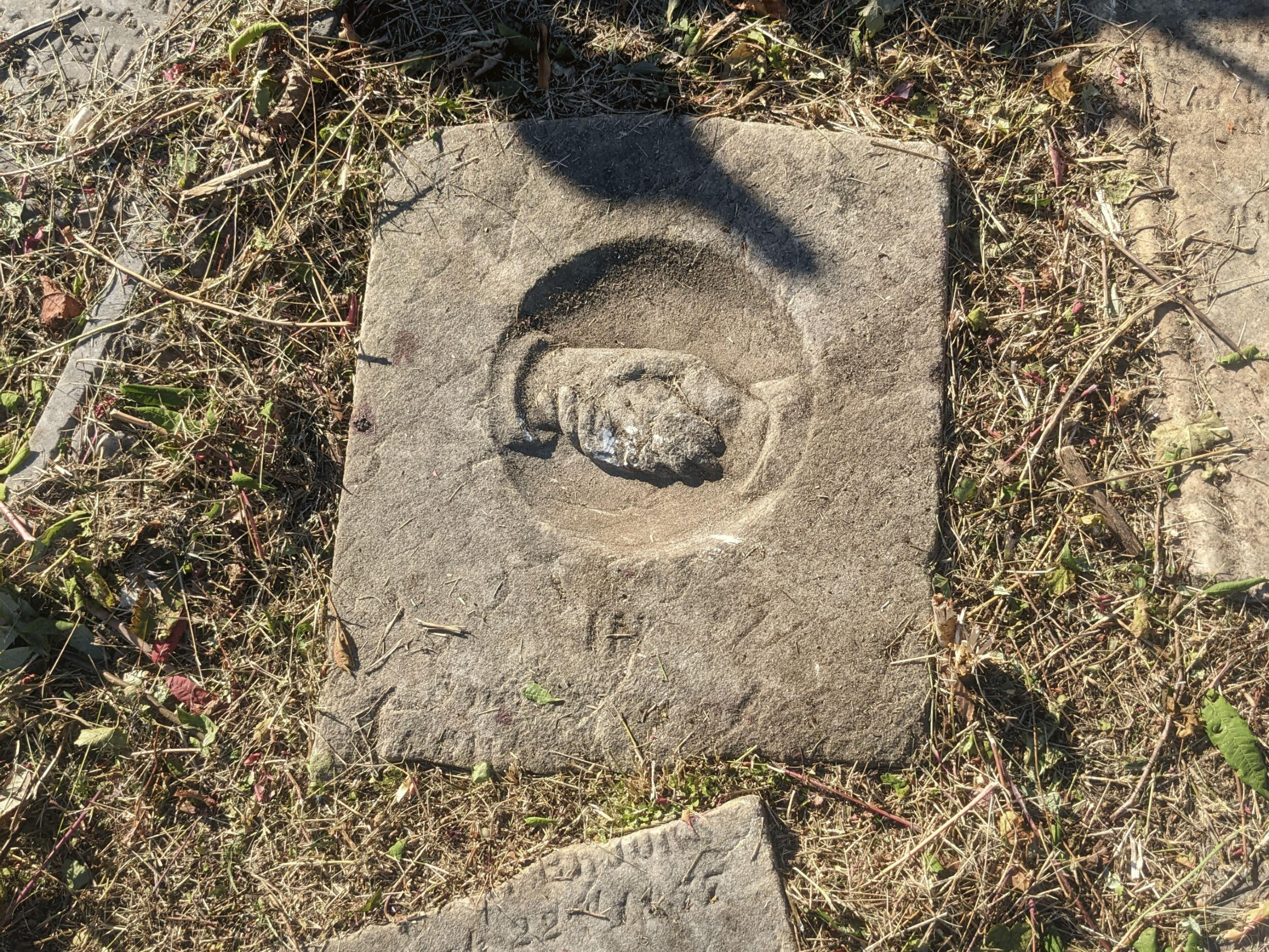 A stone on the ground with the chiseled image of hands clasped in a handshake.