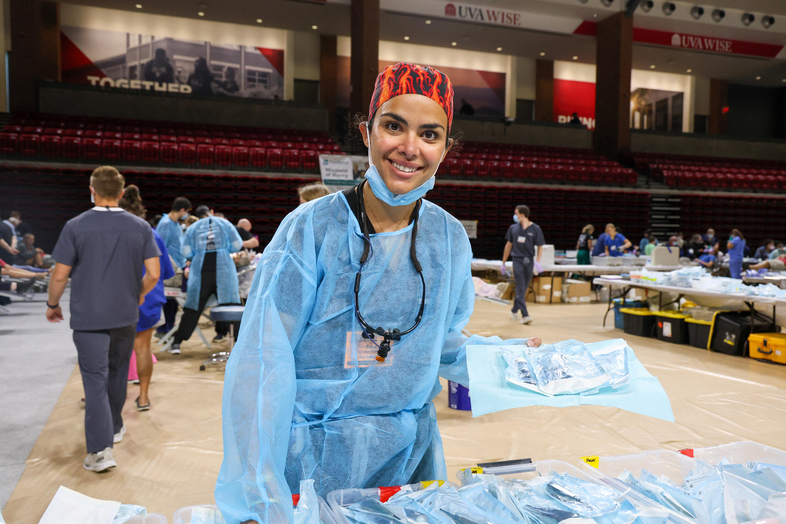 A photo of a woman in scrubs standing in a gym set up with dental chairs and equipment. 