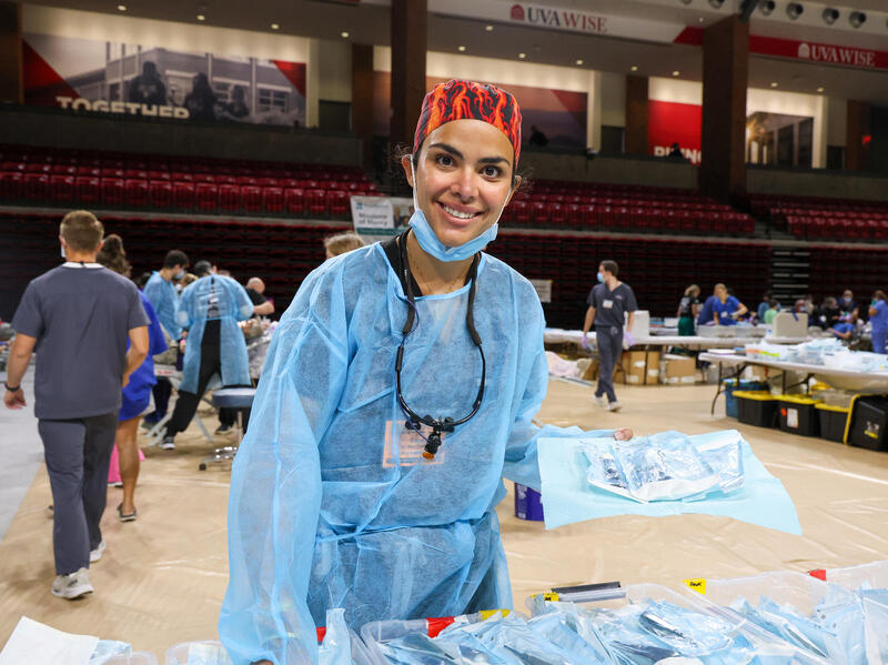 A photo of a woman in scrubs standing in a gym set up with dental chairs and equipment. 