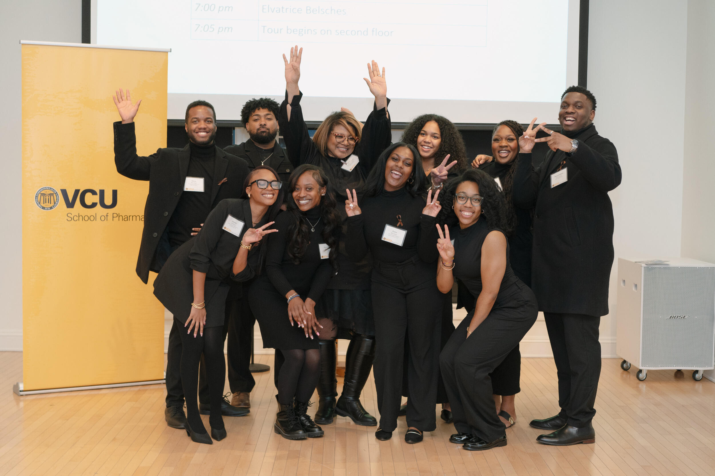 A group of men and women wearing black smile and gesture.
