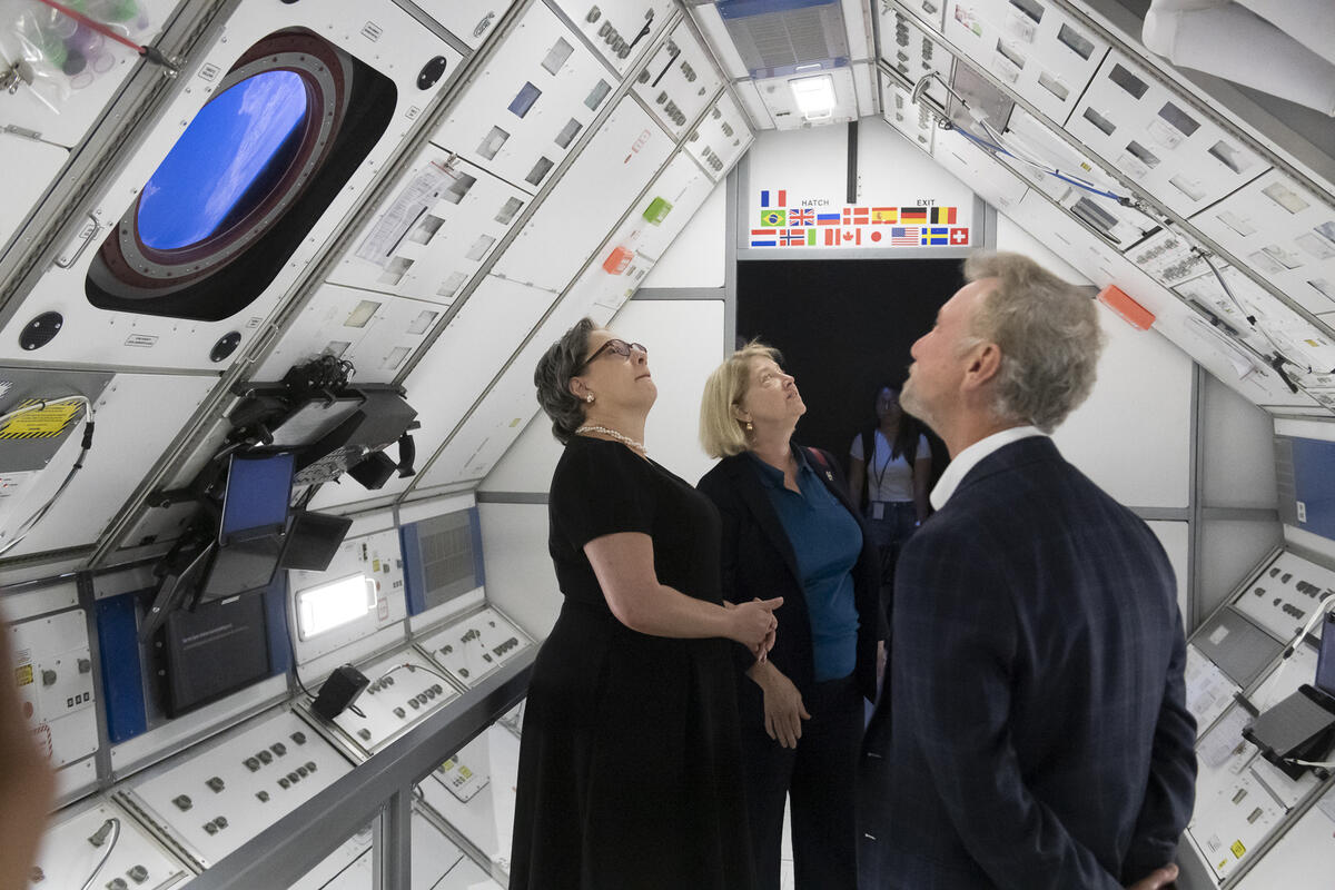 Three people standing in a model space station room. 