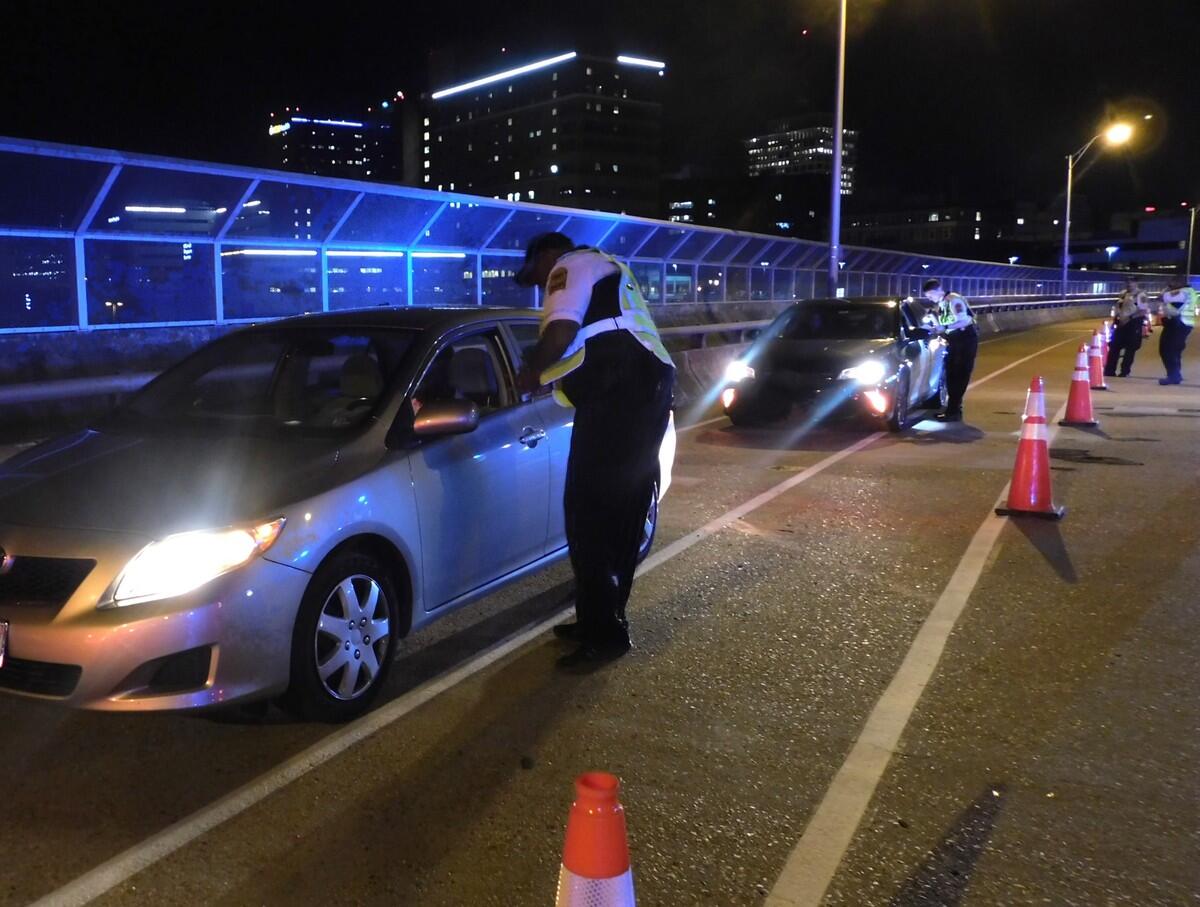 A photo of two cars that have ben stopped. At each car, a police officer is speaking with the person in the passenger side. 