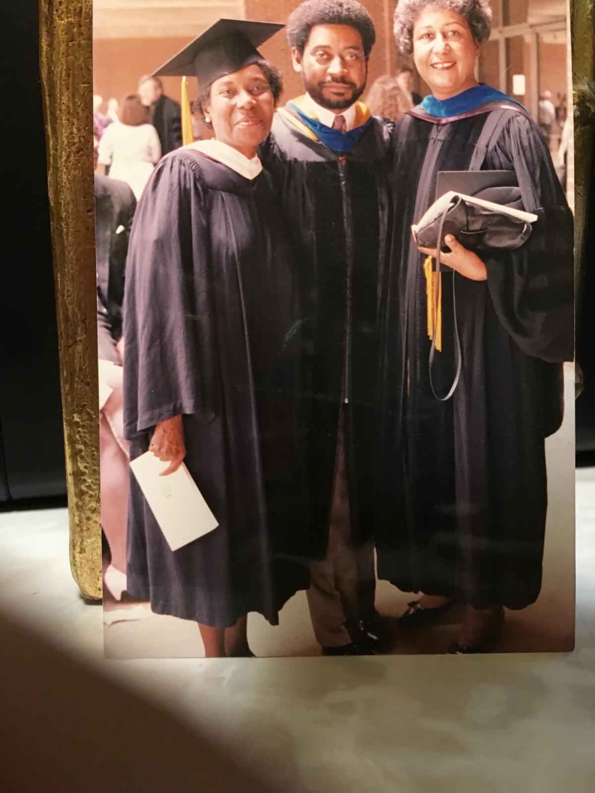 Three people in graduation gowns standing next to each other. 