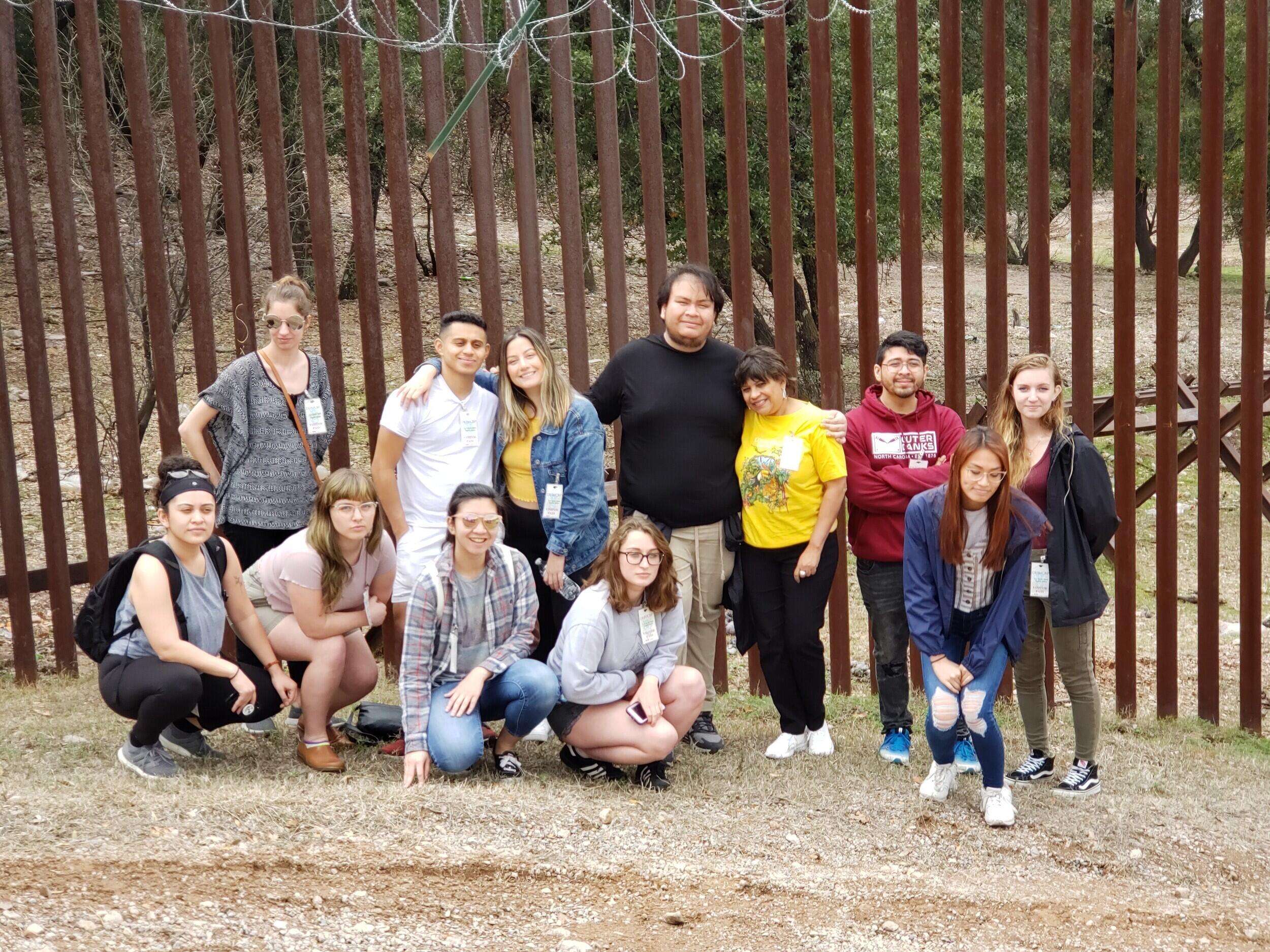 Students pose in front of the U S Mexico border wall.