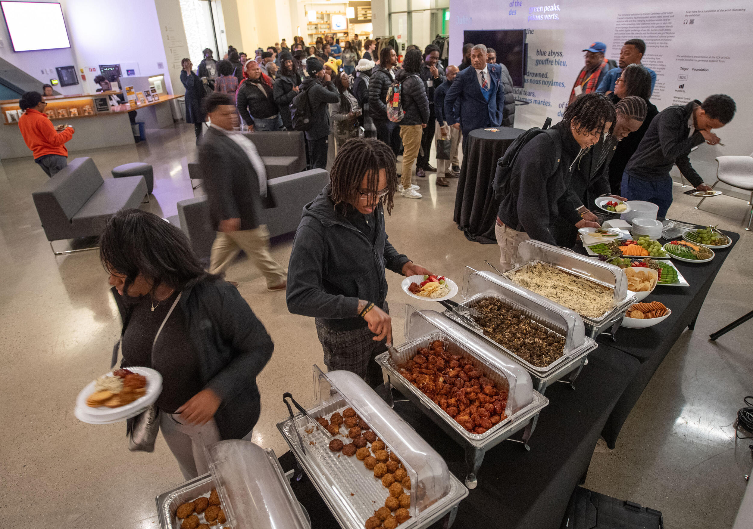 A photo of people serving themselves food from a buffet style set up. 