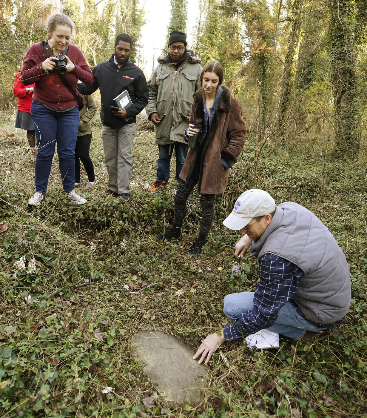 Assistant Professor Kathryn Howell, Ph.D., (left) and students look to see what Evergreen Cemetery Caretaker Ted Maris-Wolf is uncovering. 