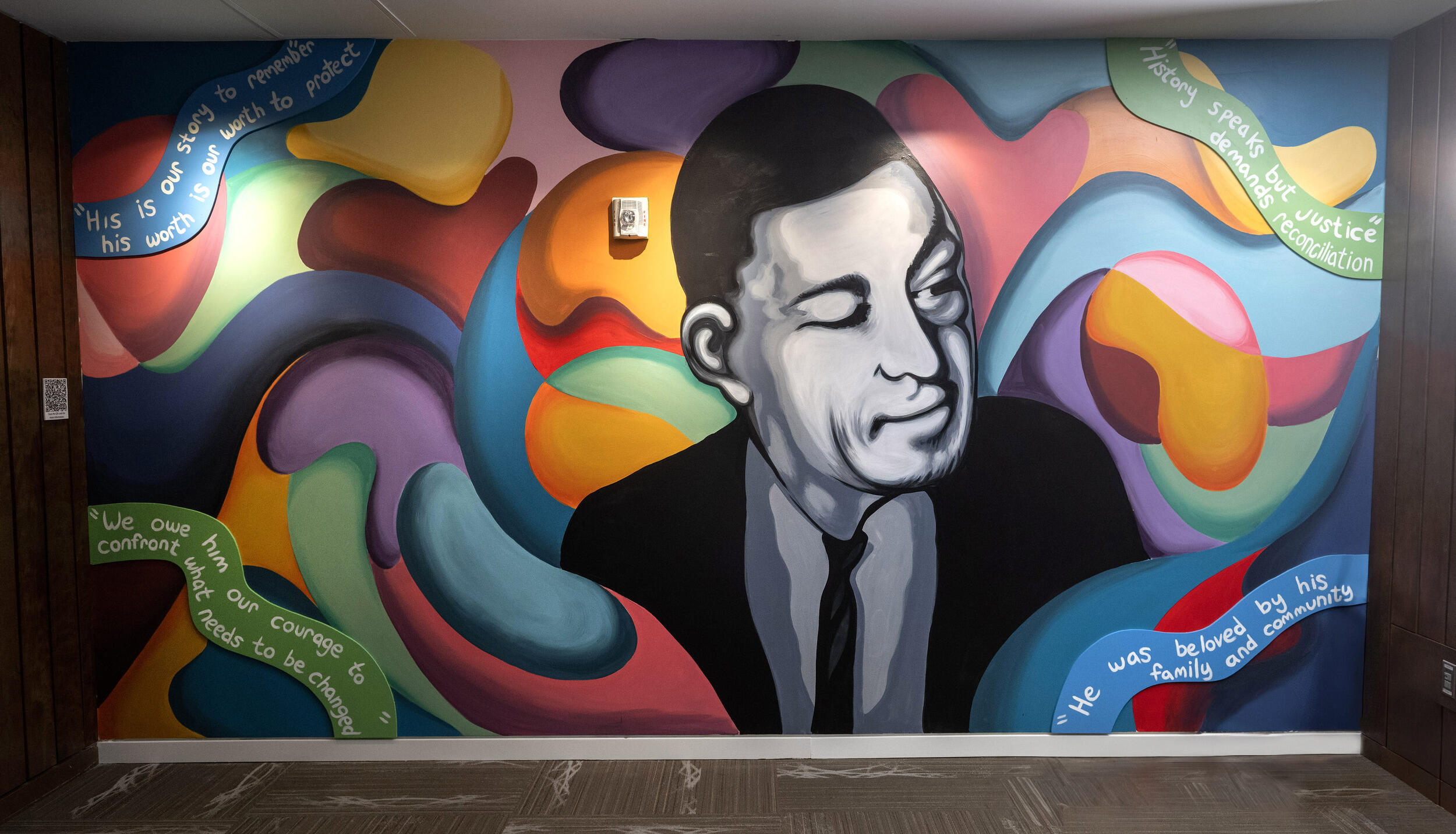 A photo of a wall mural of a black and white shaded man surounded by multi-colred, abstract shapes.