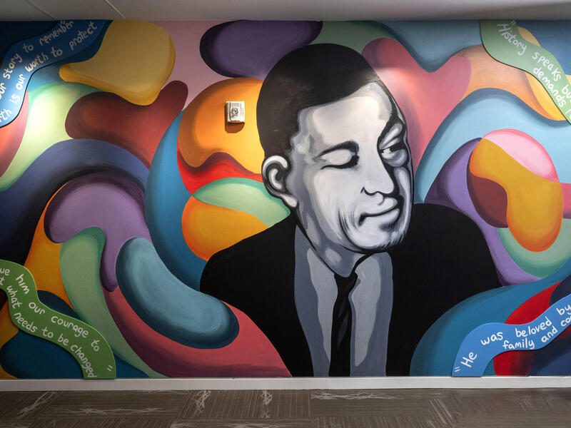 A photo of a wall mural of a black and white shaded man surounded by multi-colred, abstract shapes.