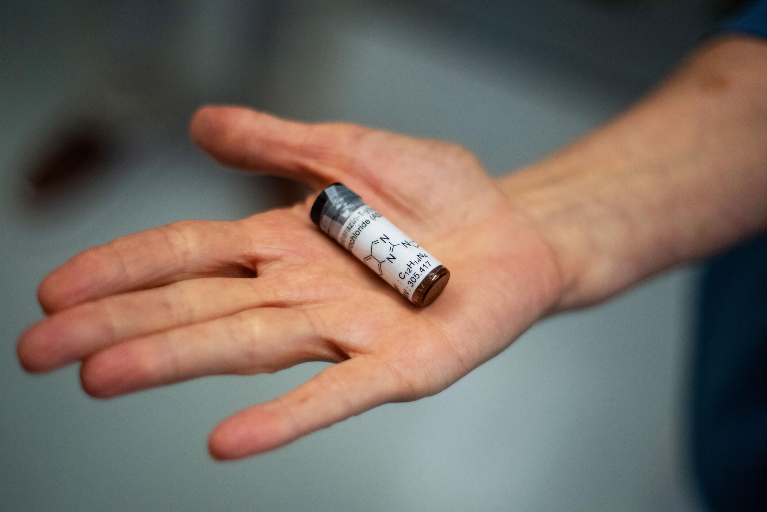 A photo of a hand holding a vial with a white label and black text on it. 