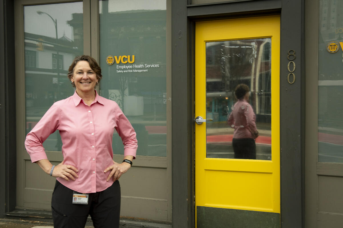A woman stading with her hands on her hips next to a building entrance with a yellow door. 