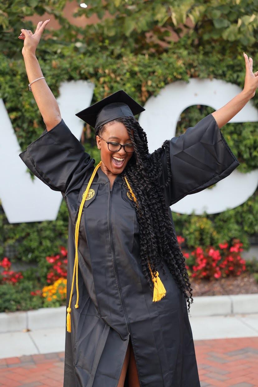 Amari Samya posing in a graduation gown and cap in front of large V C U letters.