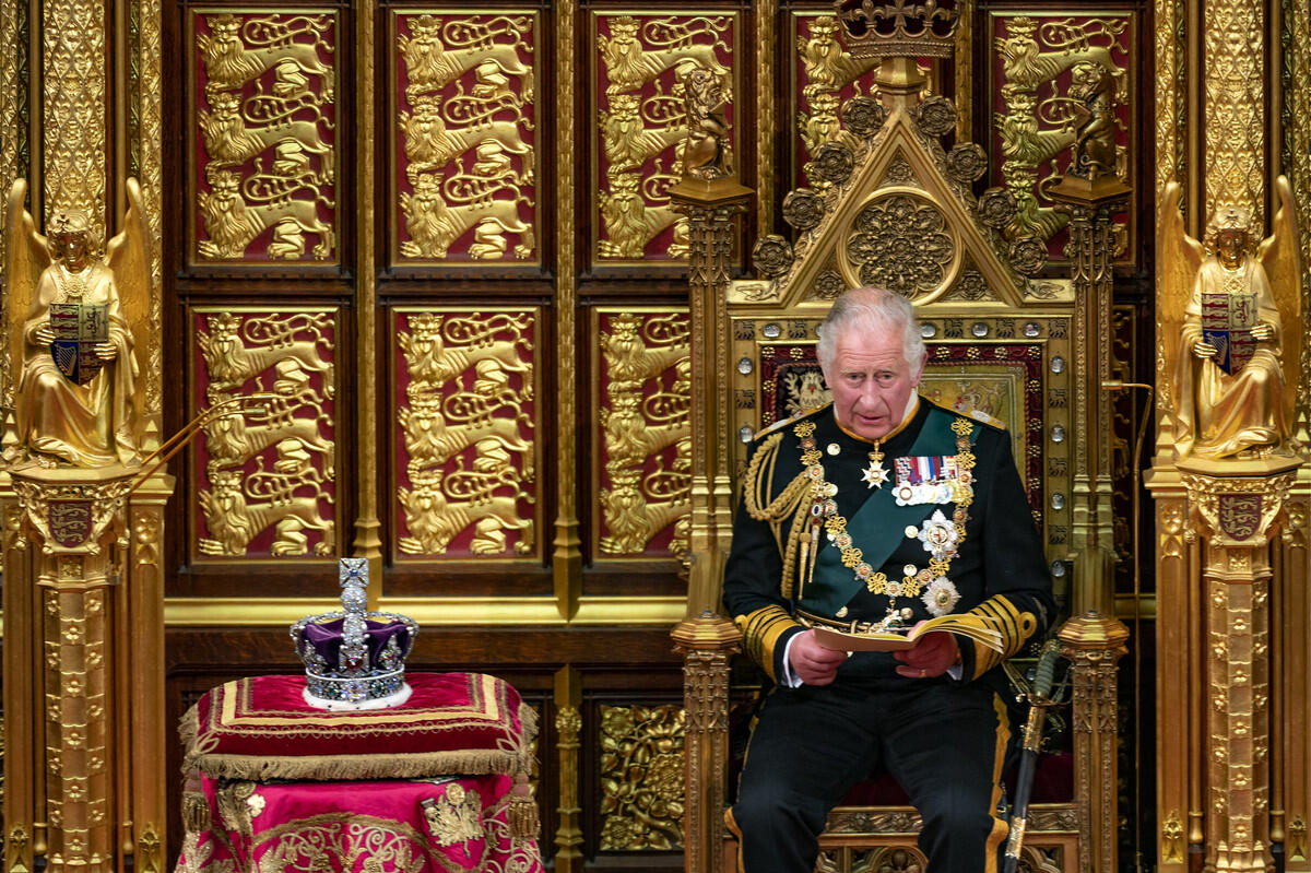 King Charles III sits on a throne with a crown resting nearby.