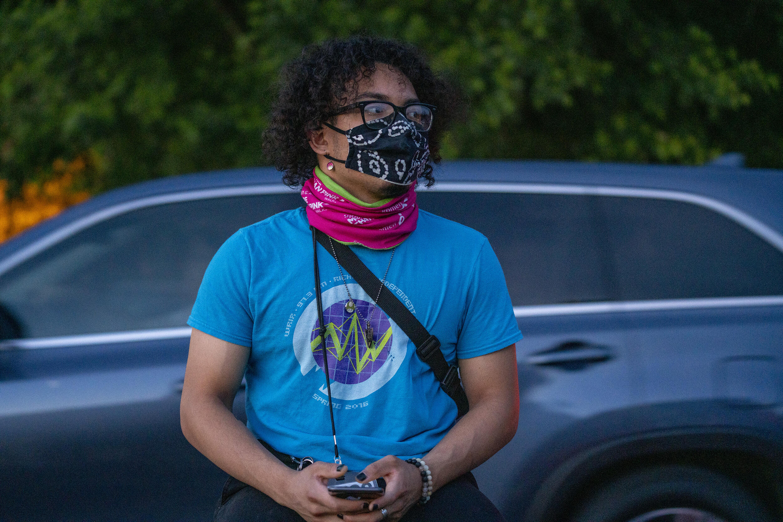 A person wearing a mask stands holding a cellphone in their hands.