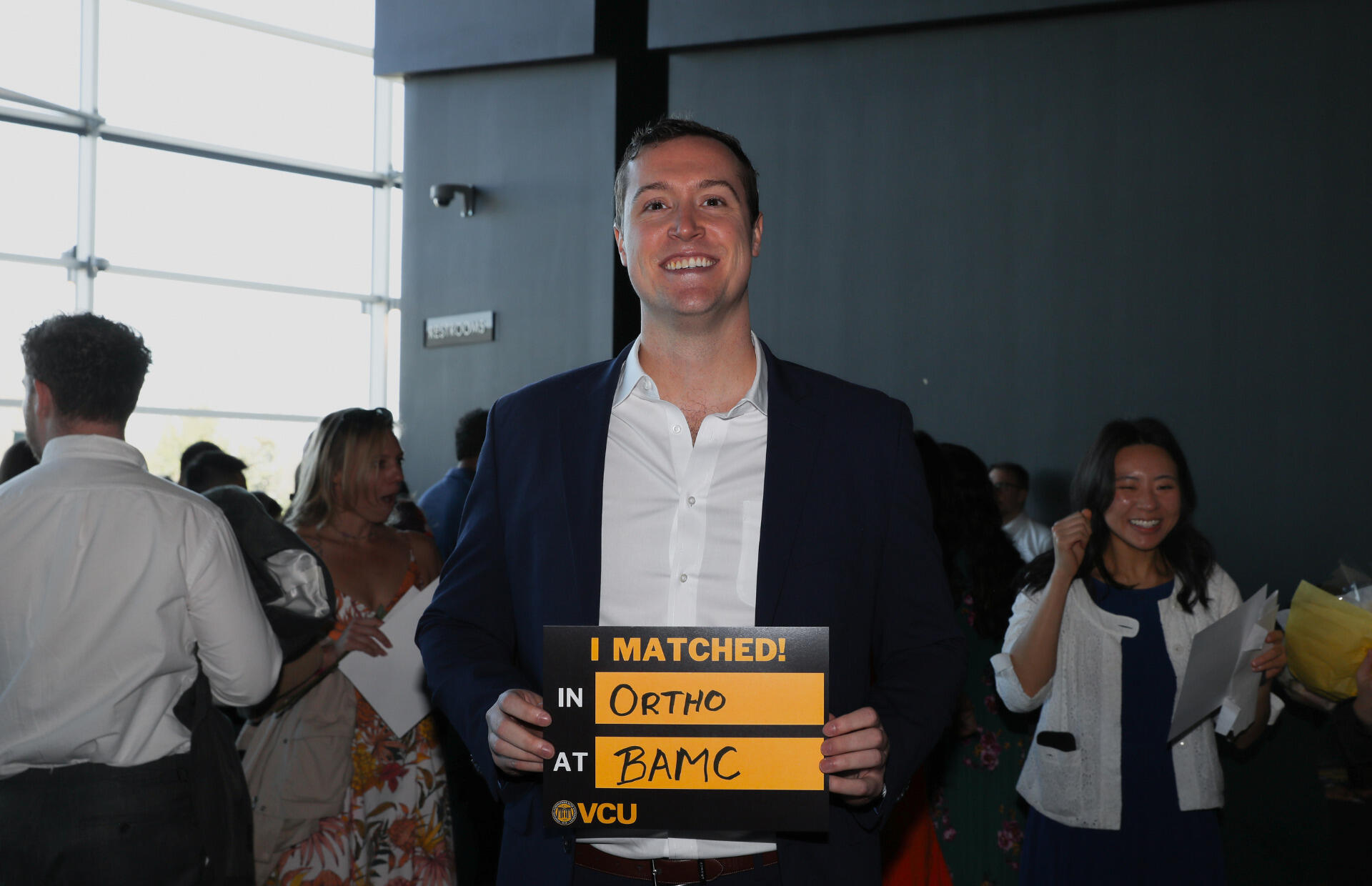 A photo of a man holding a sign that says \"I MATCHED!\" \"IN ORTHO\" \"AT BAMC\"