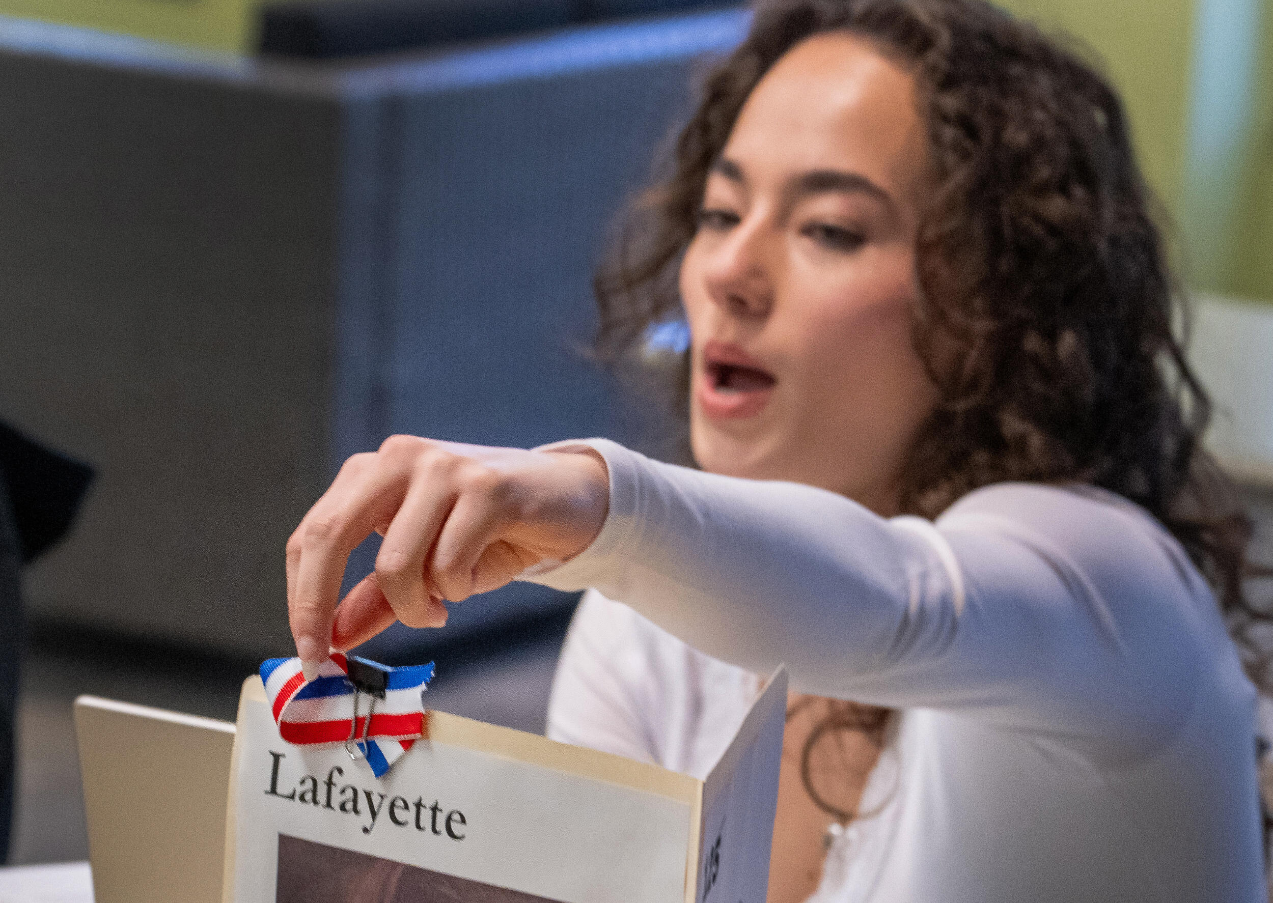 A woman reaches for a small red, white and blue ribbon attached to a piece of paper.