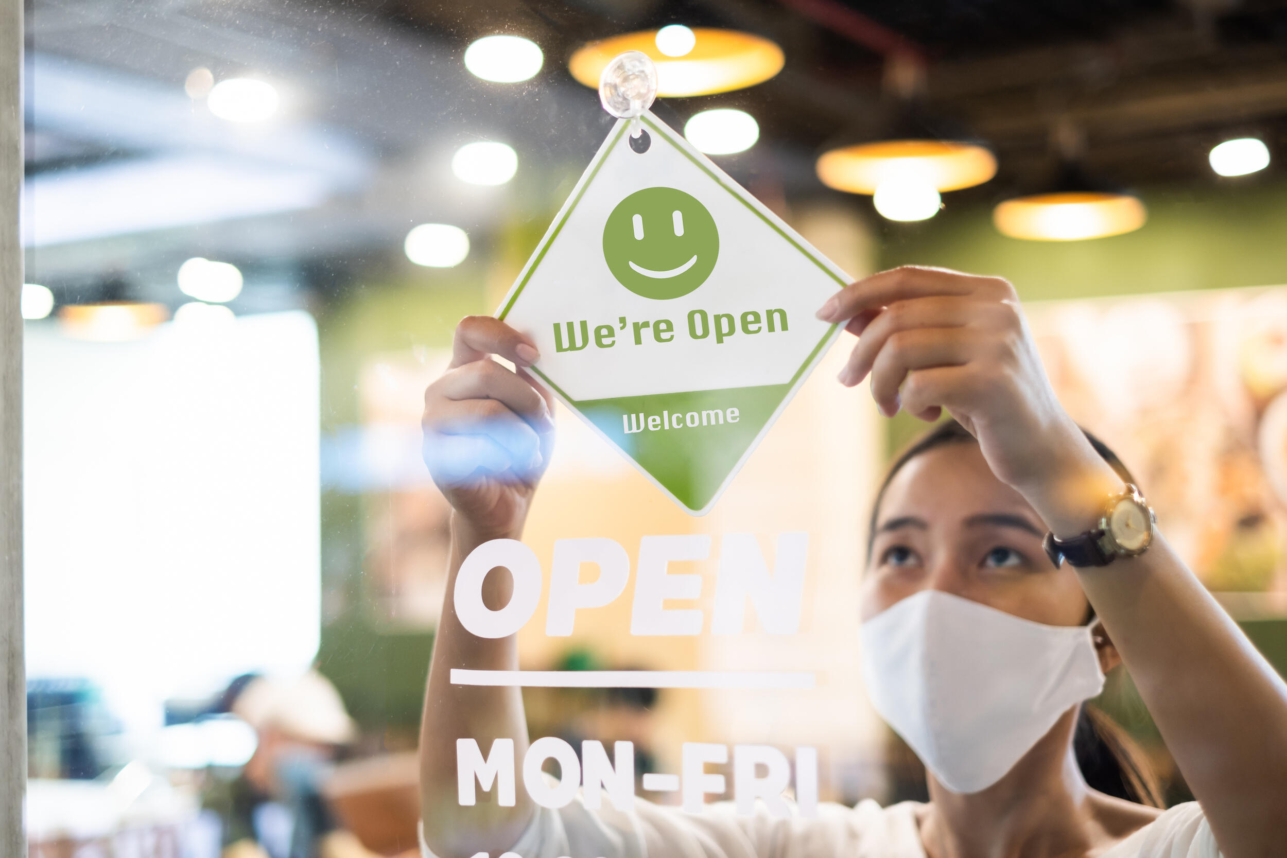 A person wearing a mask hangs a sign indicating a business is open.