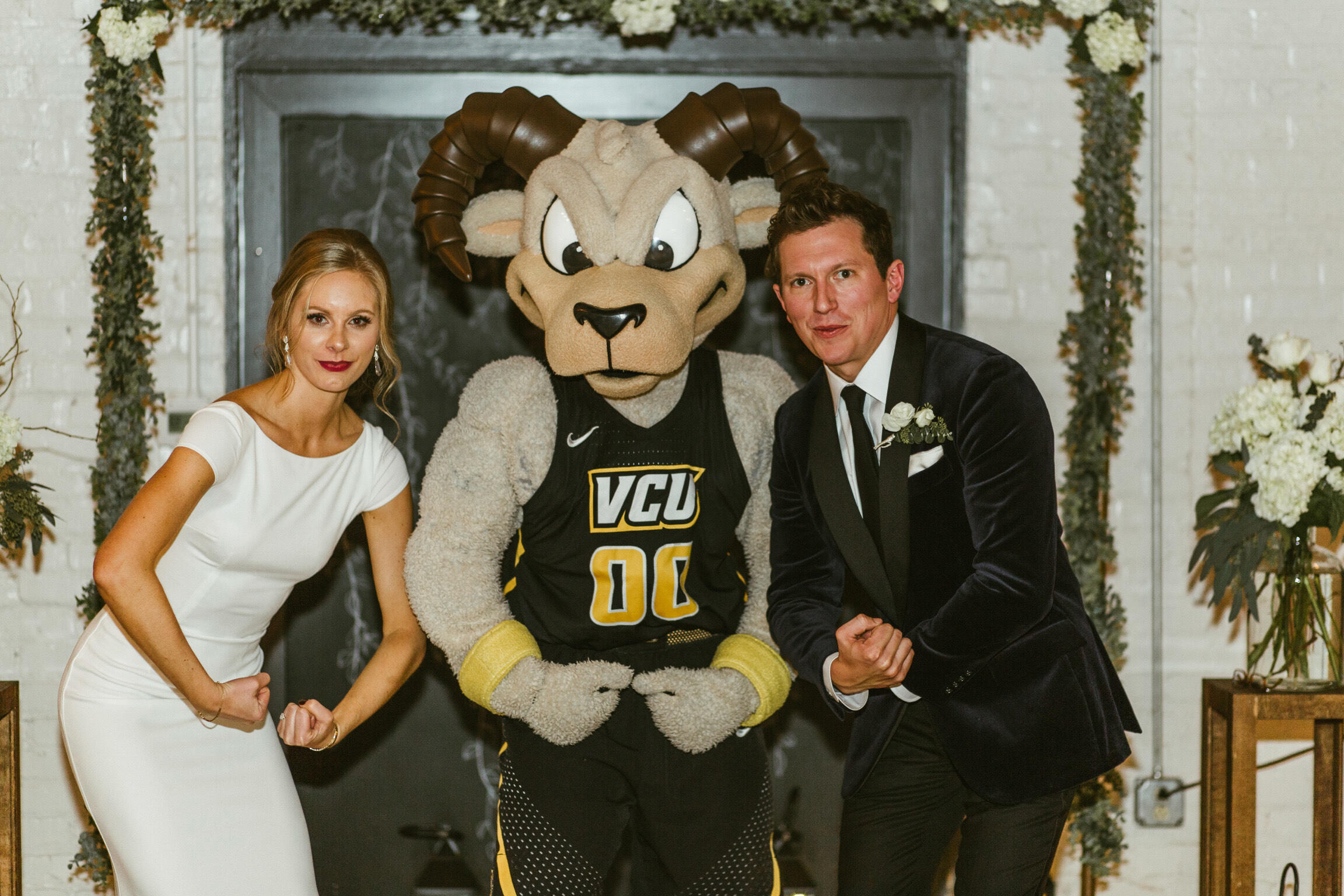 A Rodney the Ram mascot costume between a bride and groom. 