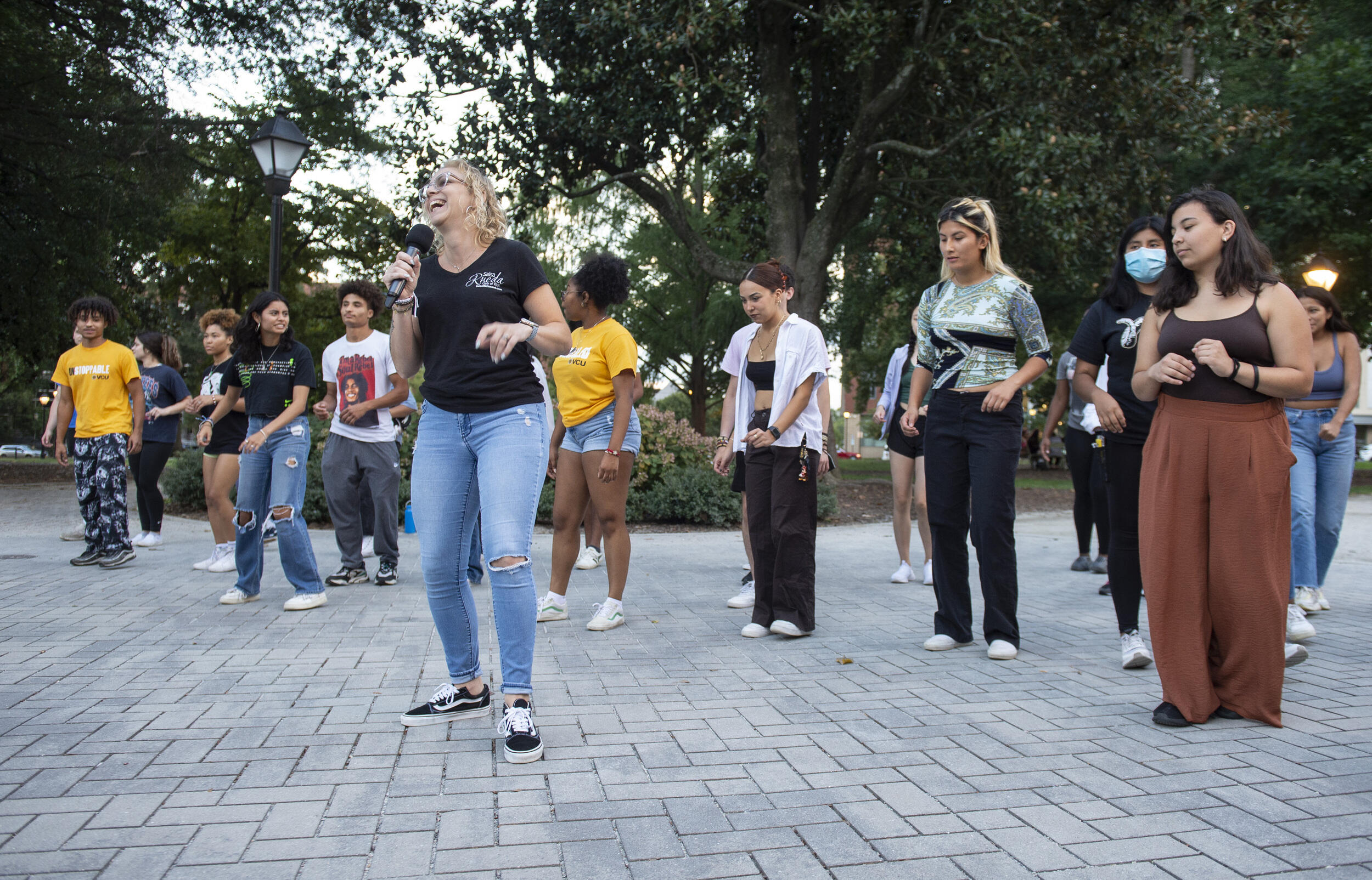 A woman holding a microphone in front of a group of students standing behind her 