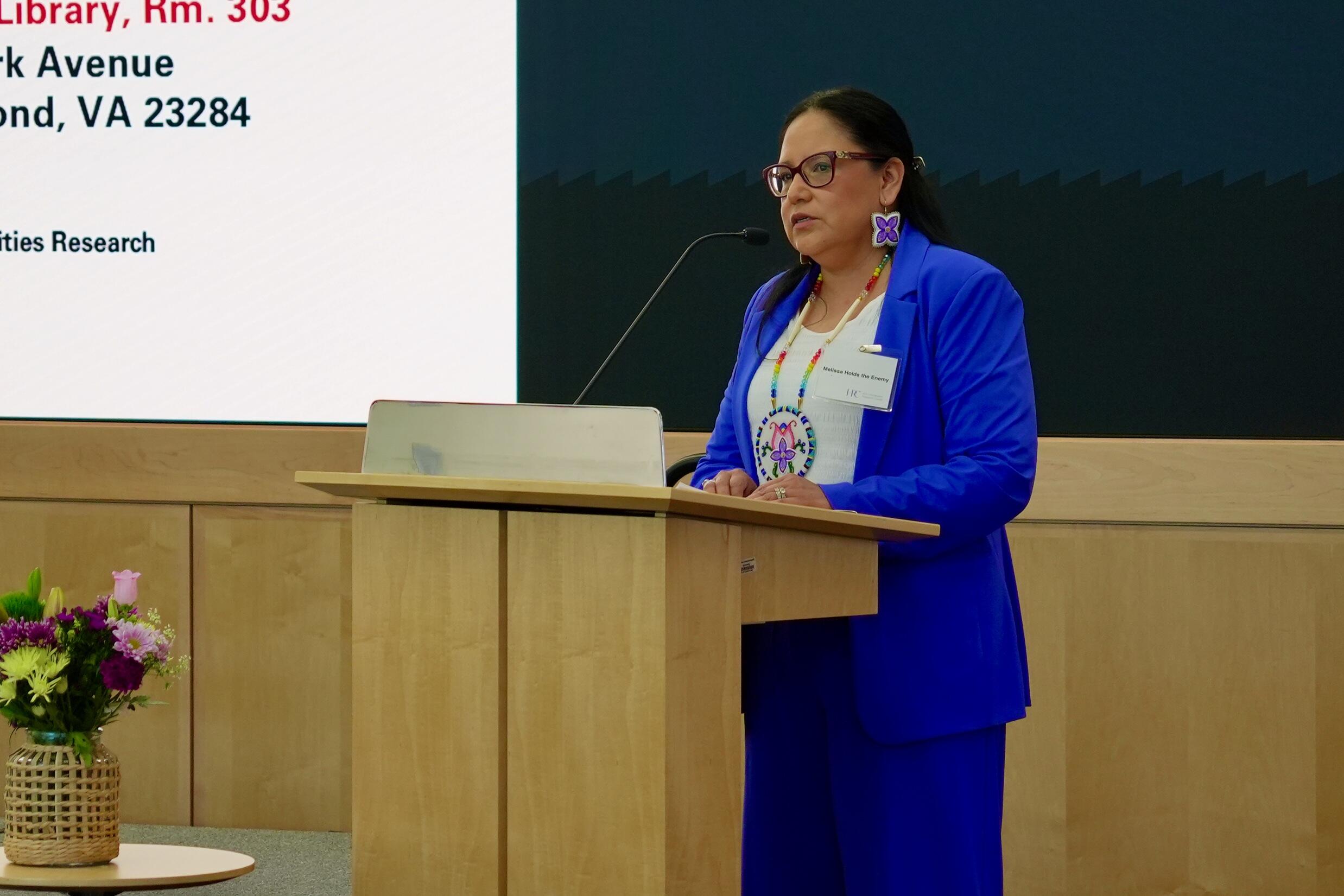 A photo of a woman standing behind a podium and speaking. 