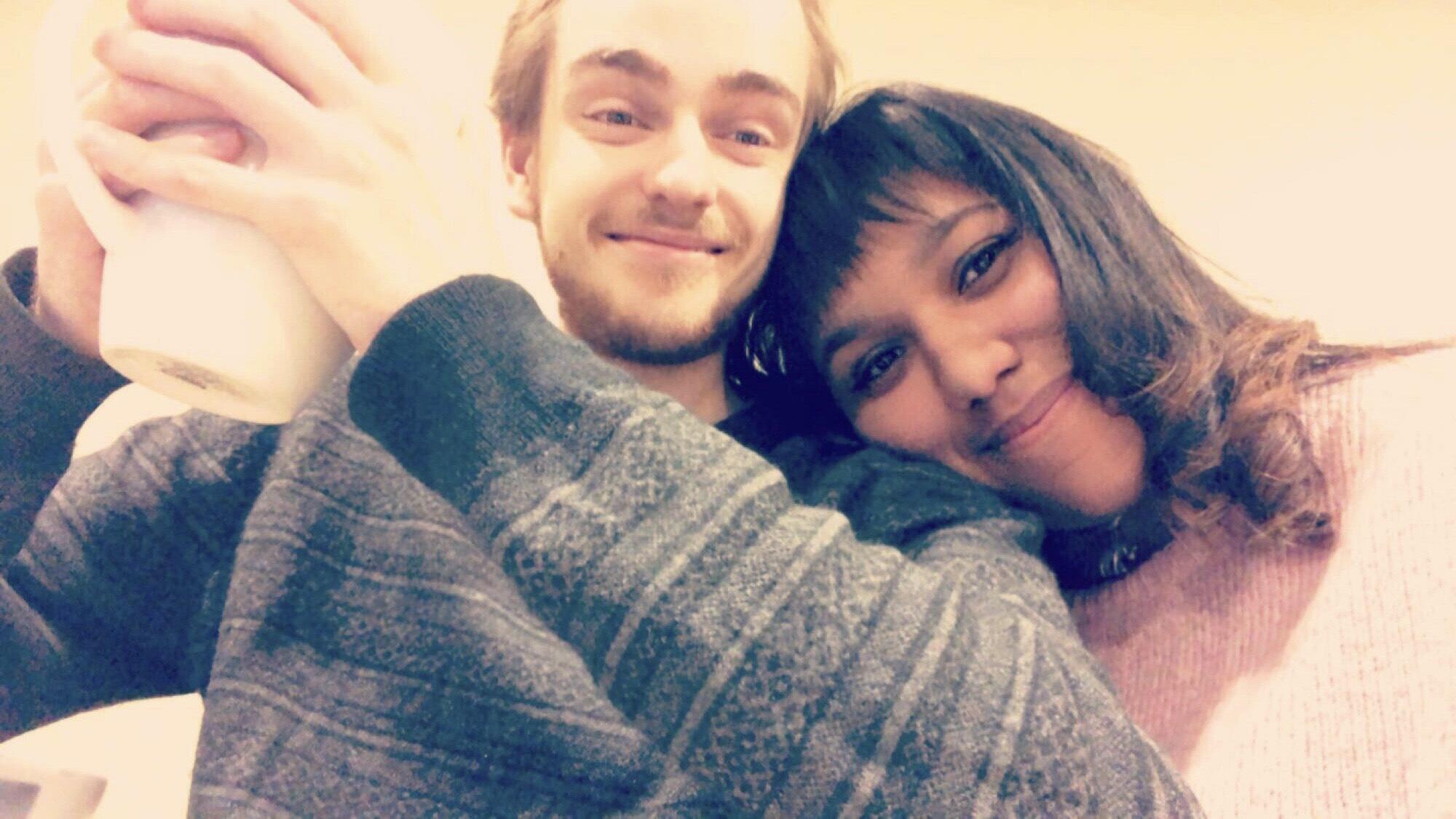 A photo of a man holding a cup of coffee and a woman resting her head on his shoulder. 