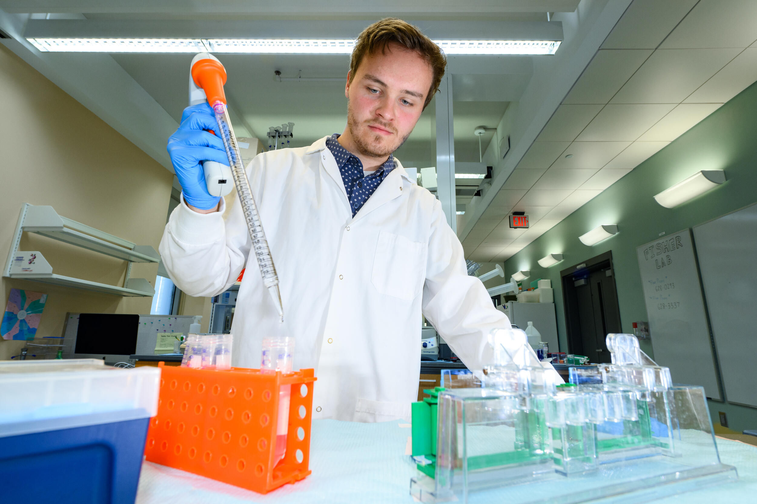 A photo of a man in a white lab coat standing in front of beakers
