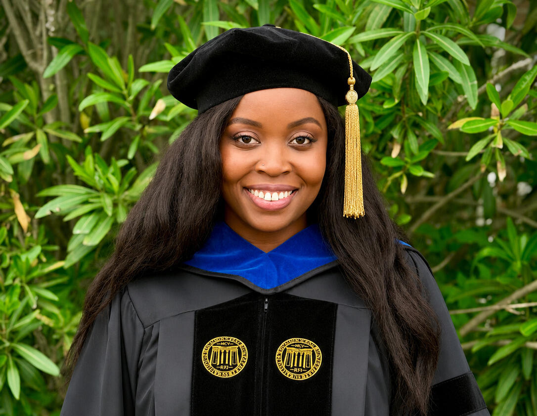 A woman smiling in graduation cap and gown attire.