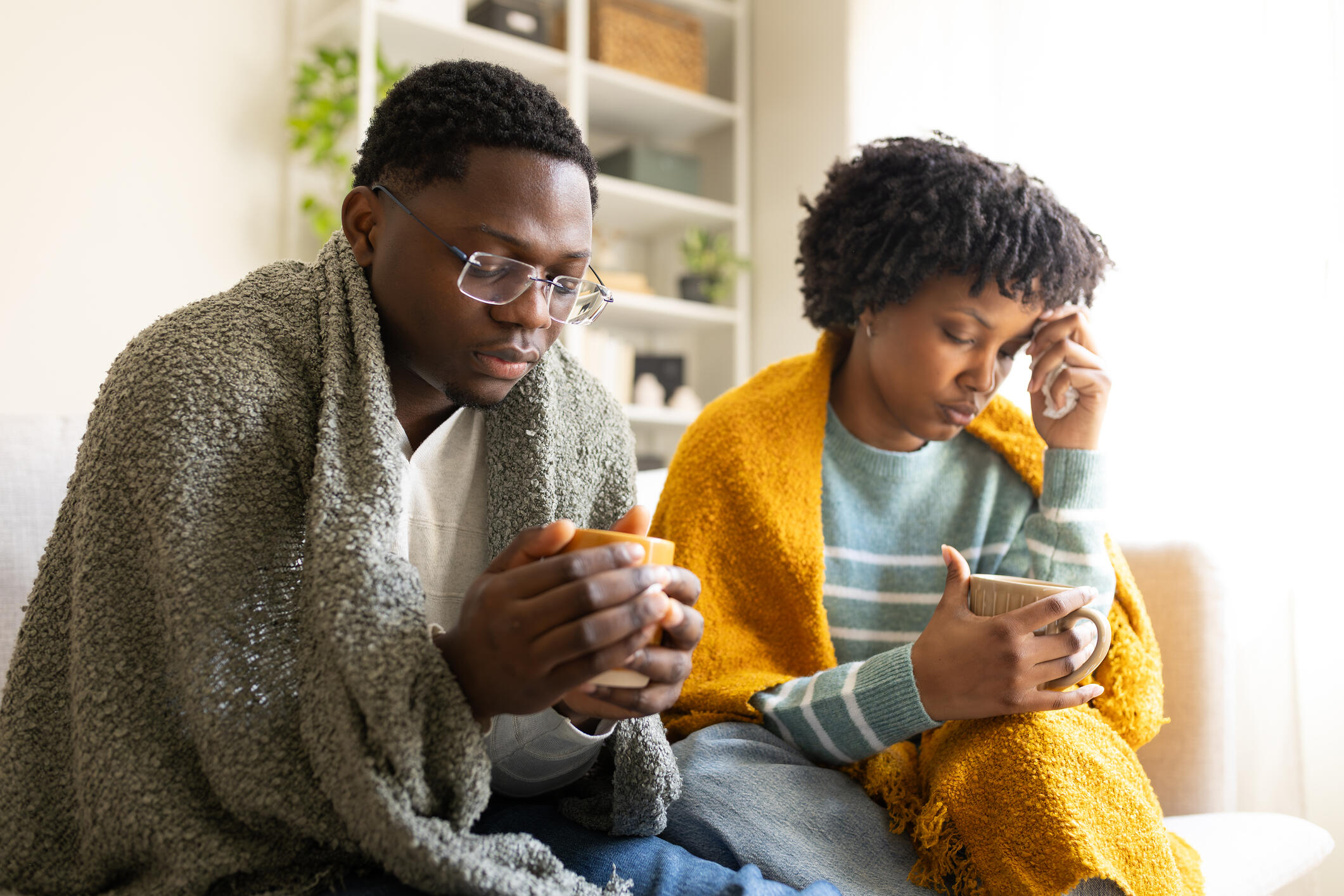 A man and a woman have blankets over their shoulders for warmth, appearing to feel ill, illustrating the pain experienced by sickle cell disease patients.