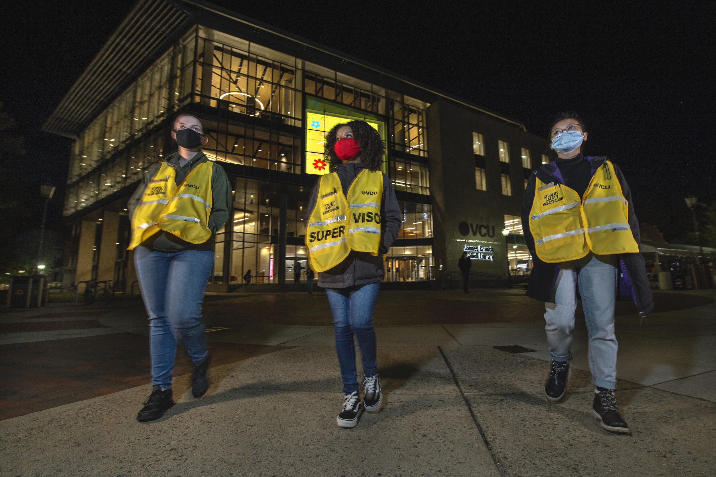 Three students wearing safety vests pictured at night.