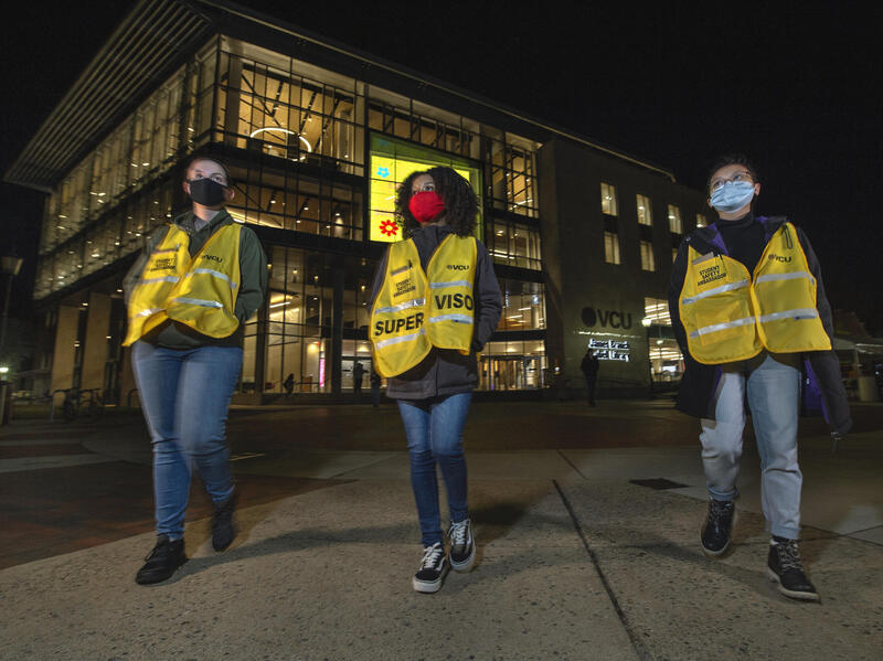 Three students wearing safety vests pictured at night.