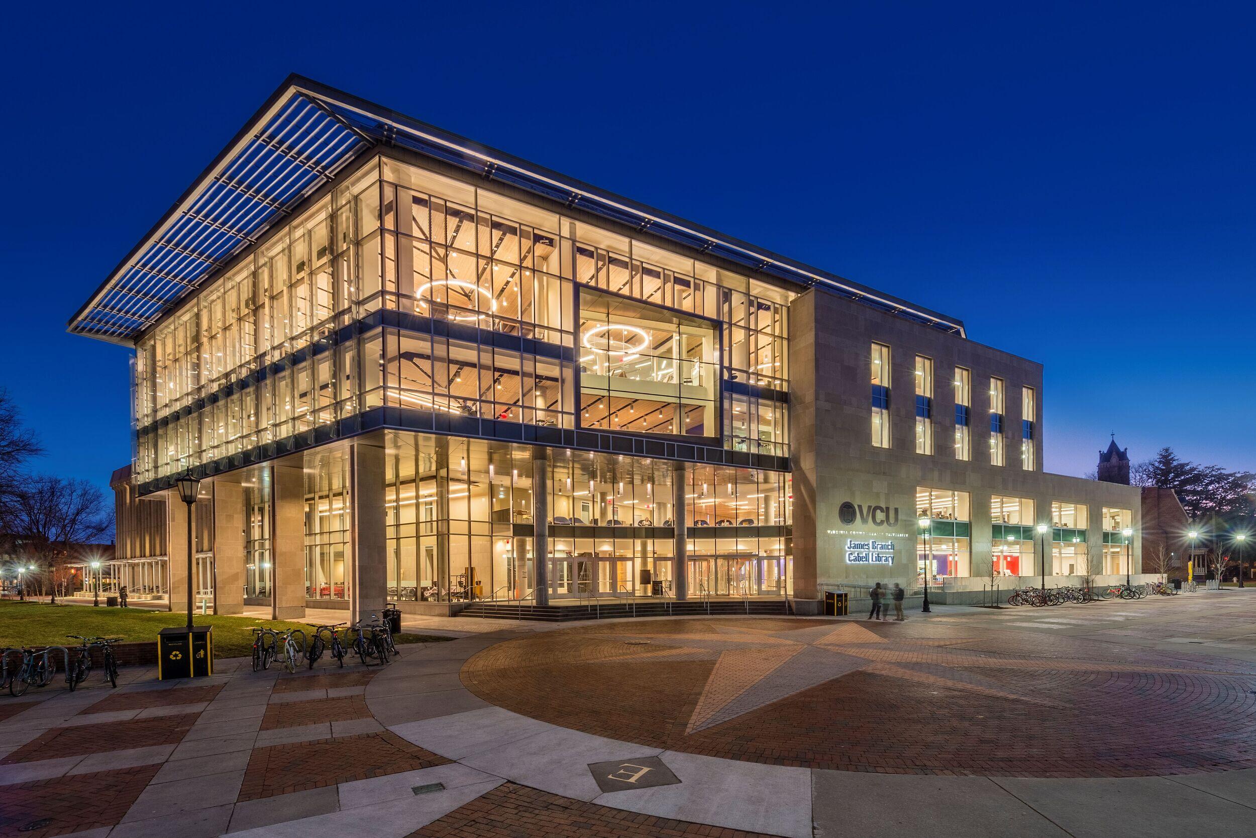 A photo of the entrance of James Branch Cabell Library lit up against a dark blue sky. 