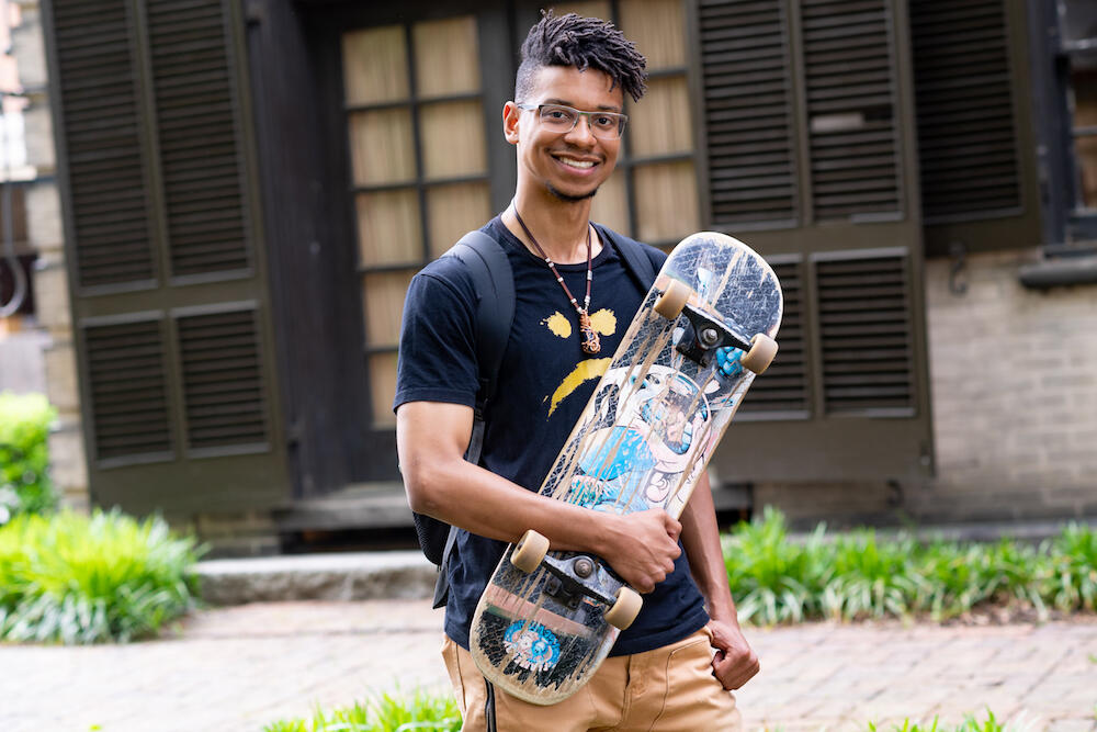 A smiling person stands while holding a skateboard.