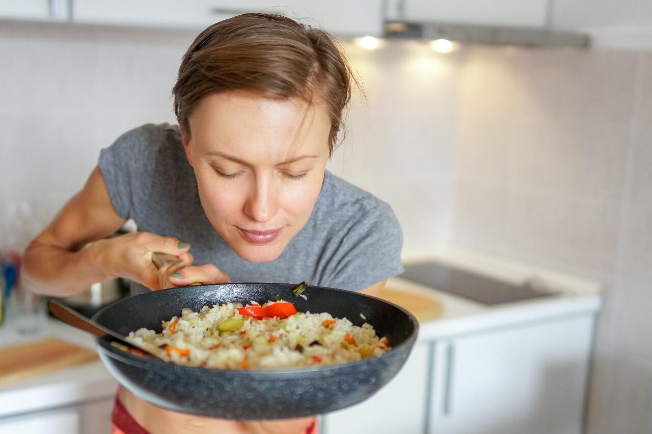 A person smells food cooking in a pan.
