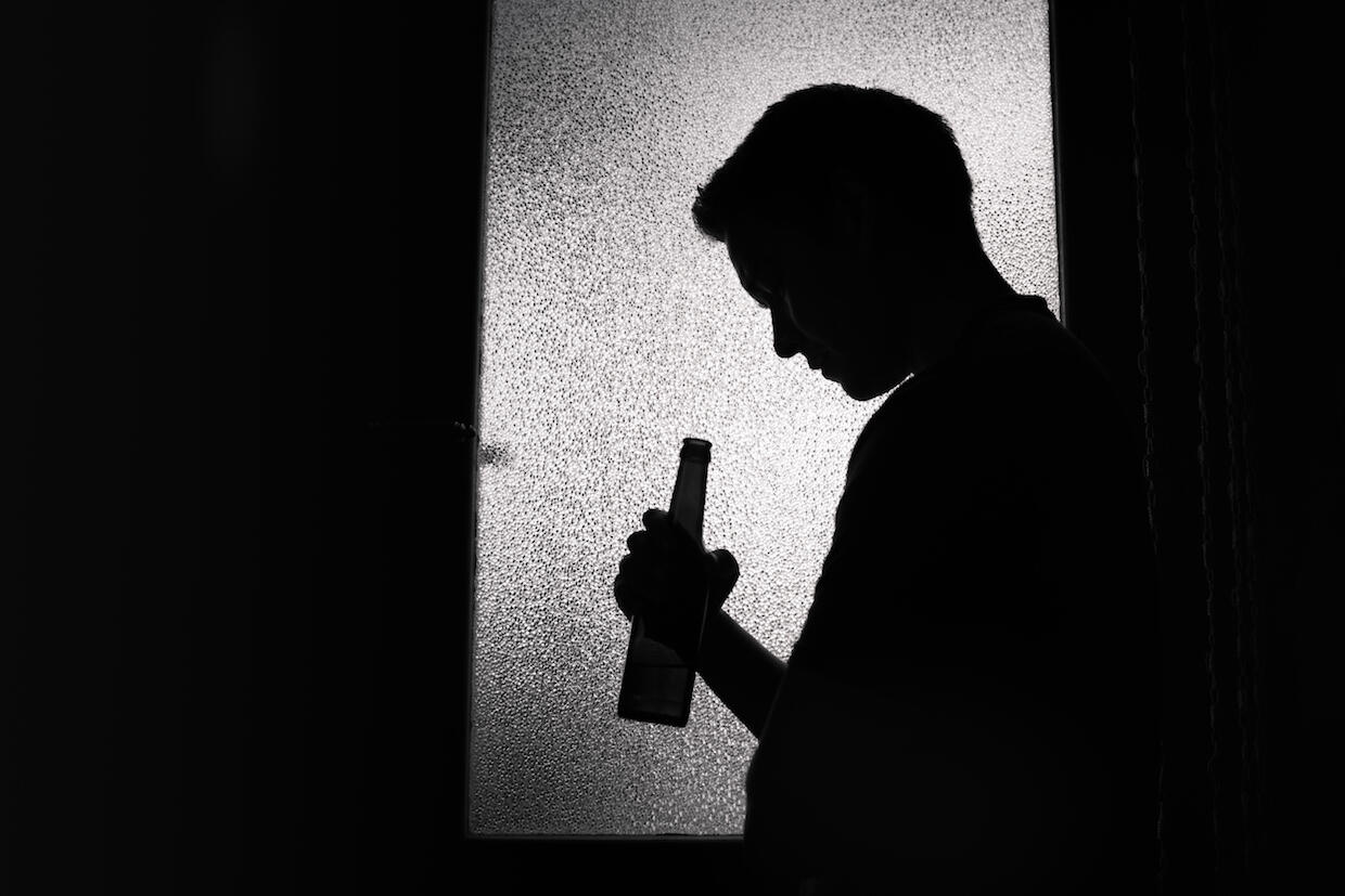 A person in silhouette holding a beer bottle. 