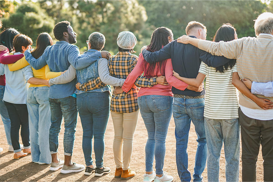 A photo of 10 people from behind. They are standing side by side with their arms wrapped around each other's backs. 