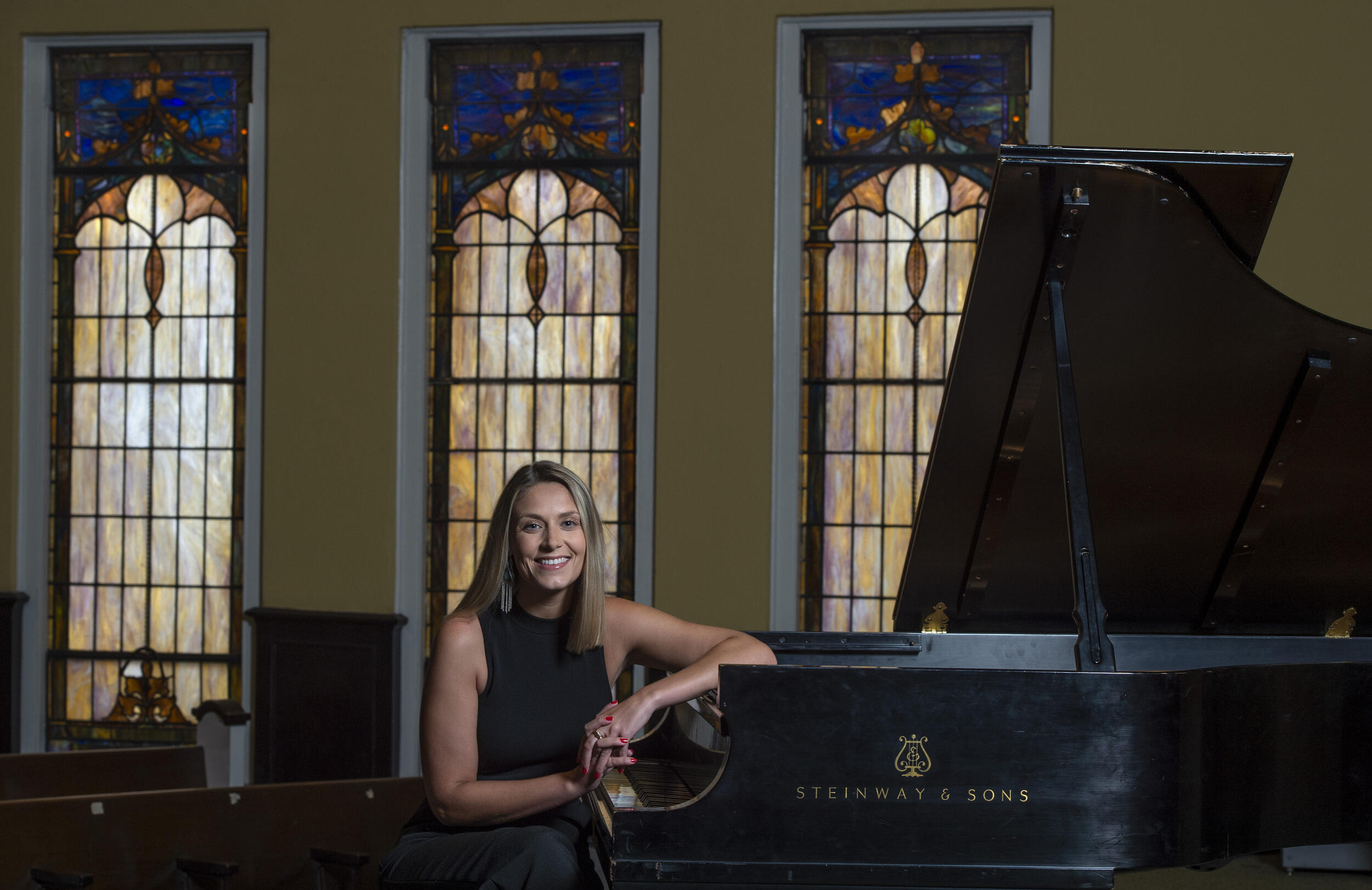Katie Cappuccio sitting at a piano with stained glass windows behind her