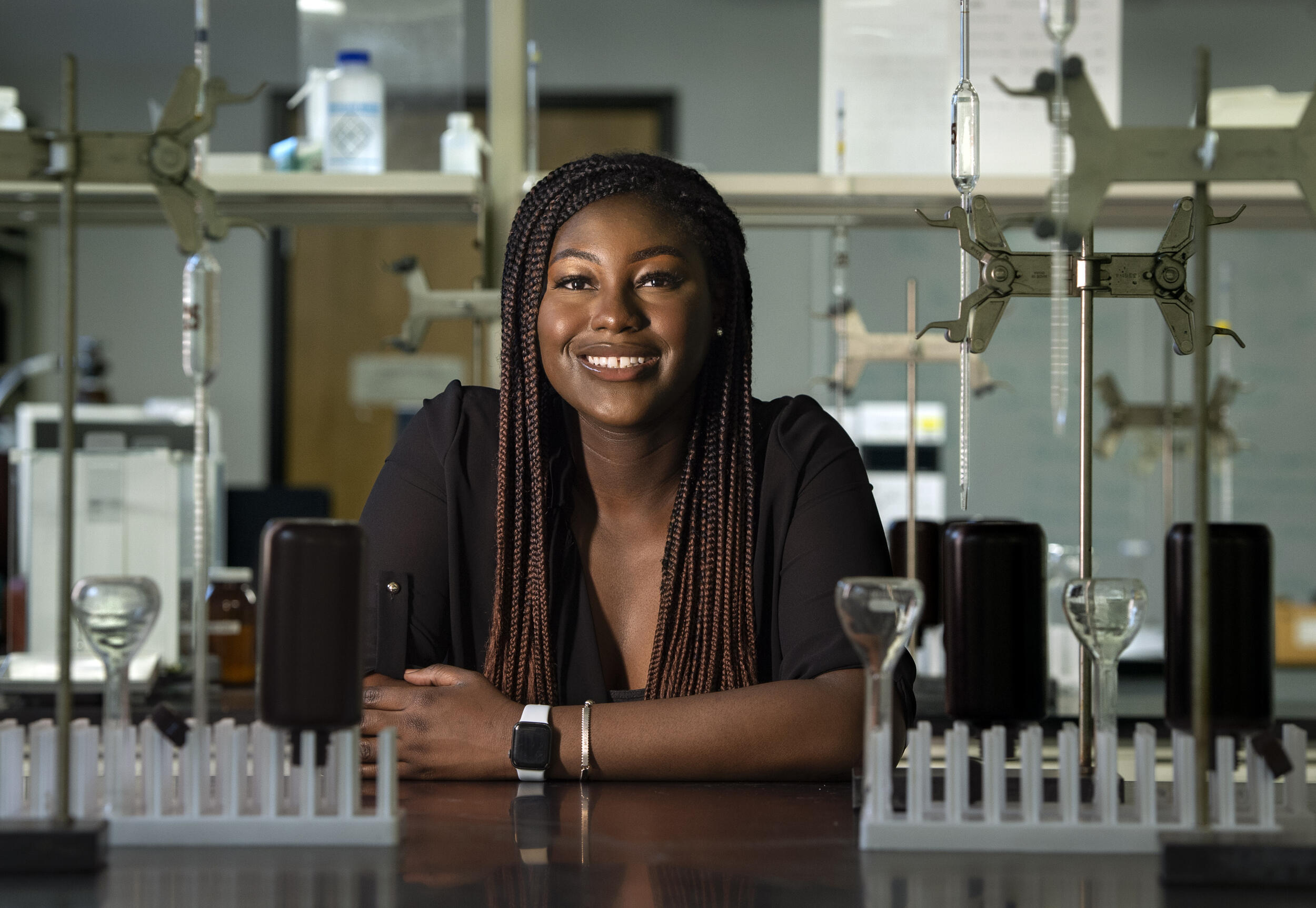 A woman smiling resting her arms on a table. All around her is scientific equipment