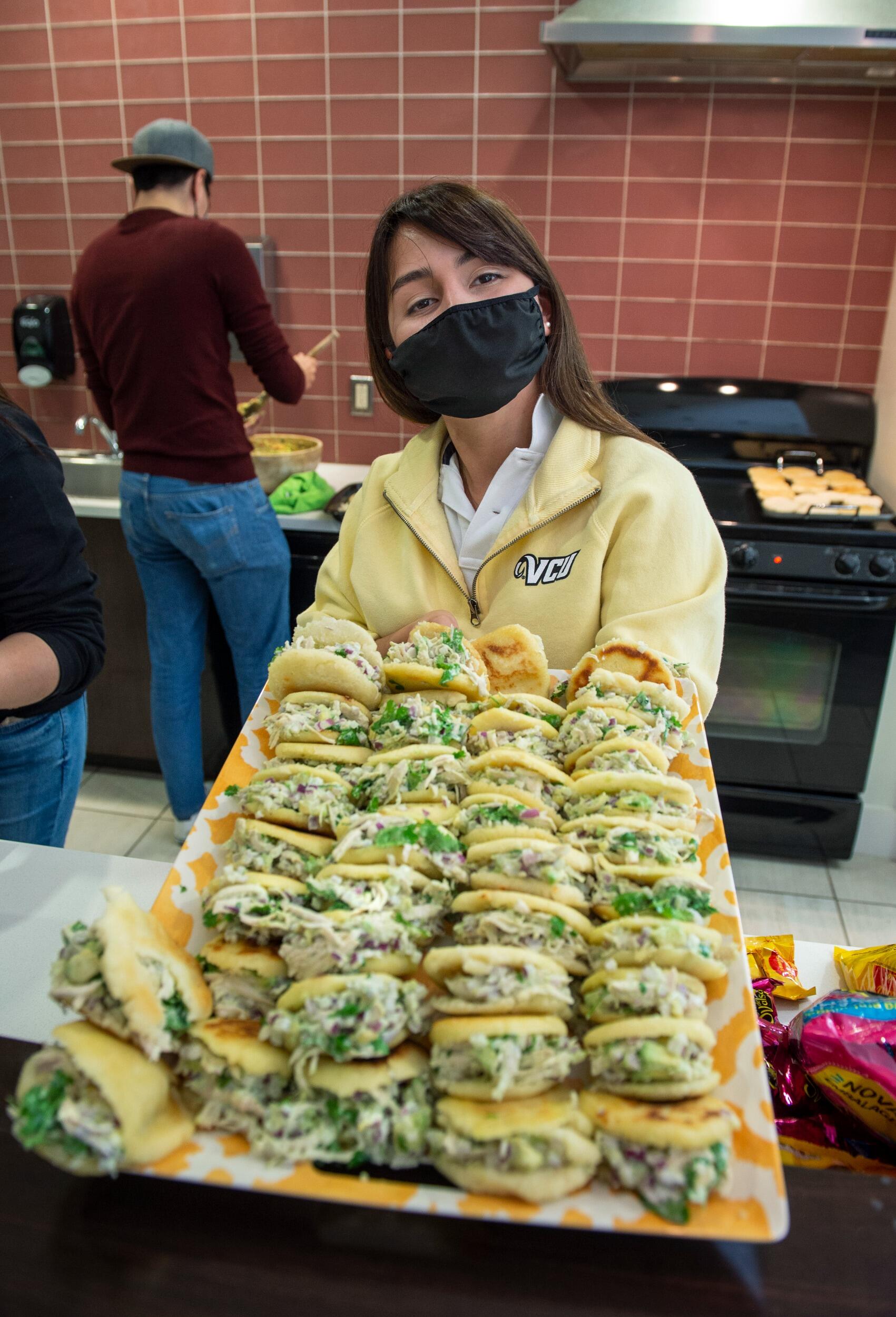 Student in mask holding a tray of arepas.