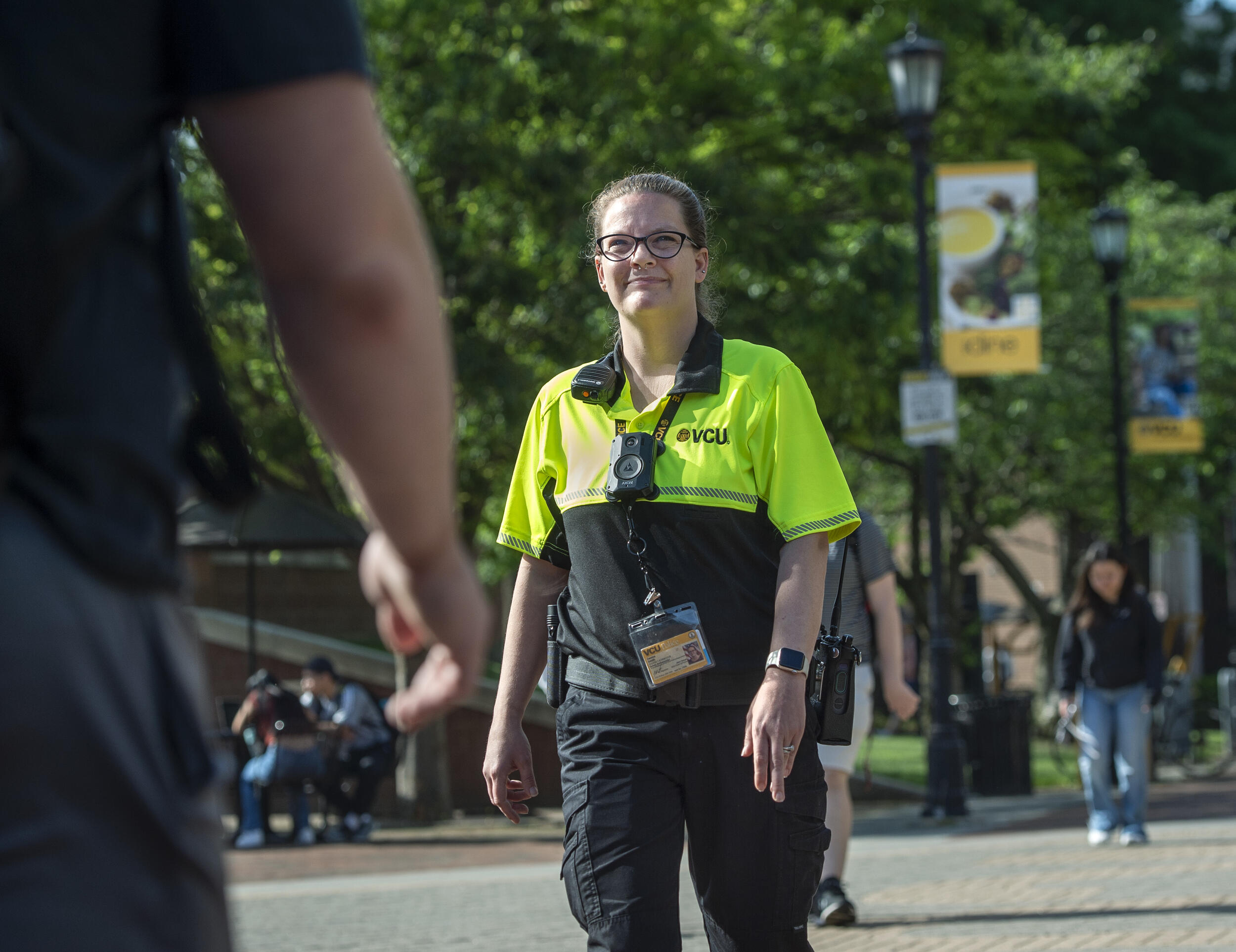 A woman wearing wearing a VCU Police uniform standing in the middle of the sidewalk in a park. 