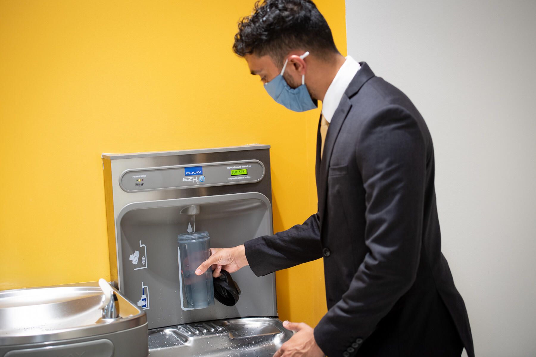a man in a suit fills a water bottle at a bottle filling station inside a VCU building